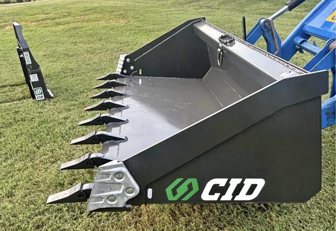 Black root rake attachment on a blue tractor, placed on grass field.