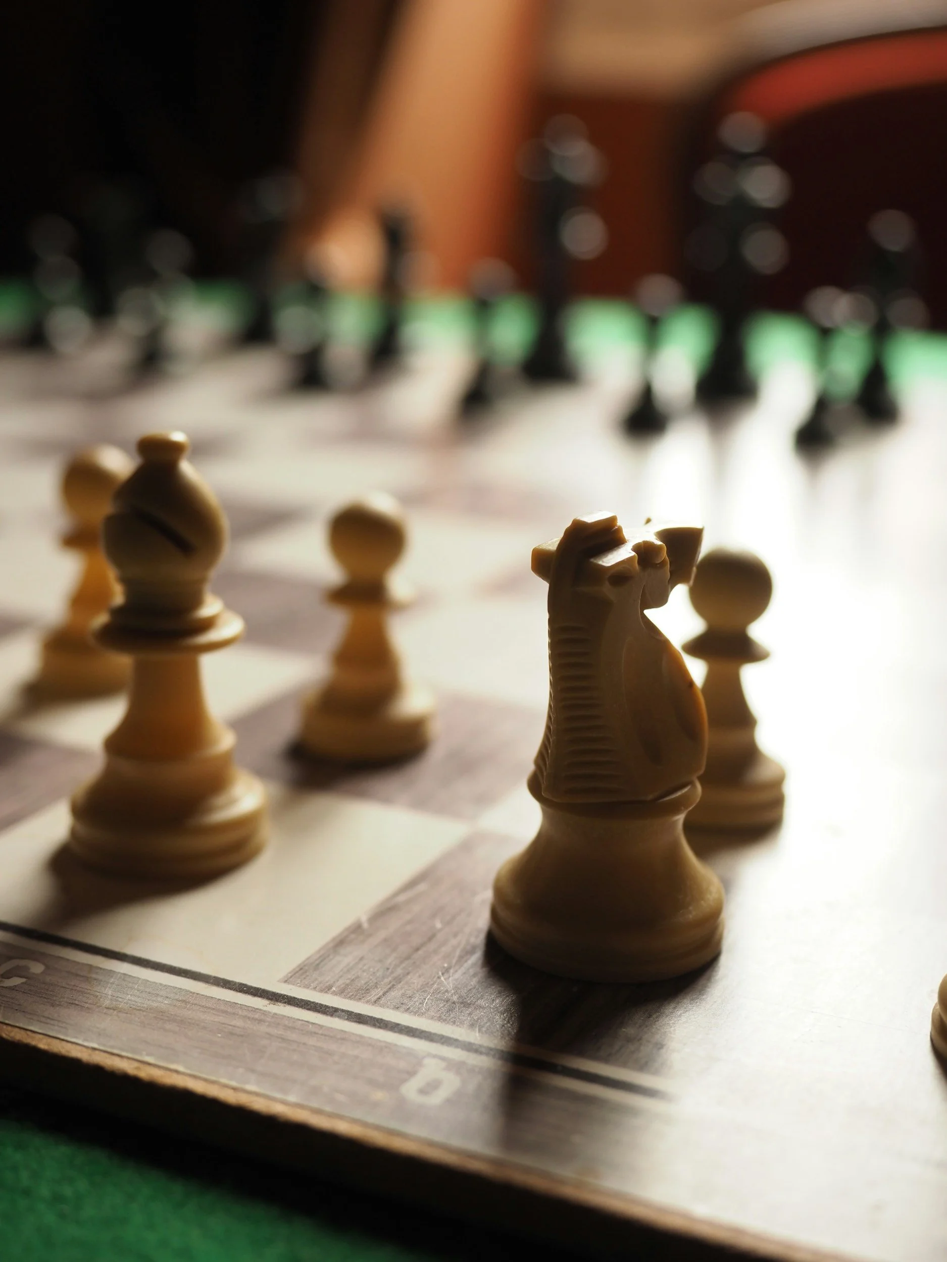 Close-up of a chessboard with white chess pieces, including a knight, in focus and the black pieces blurred in background.