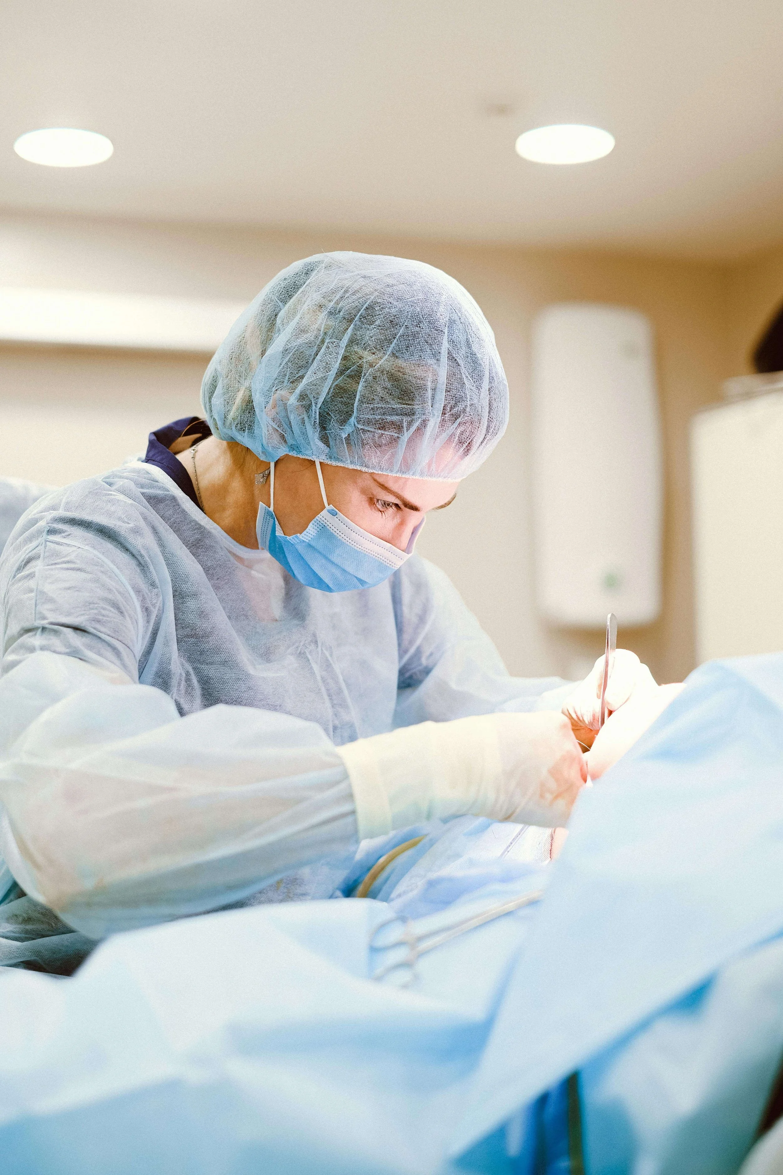 Surgeon in scrubs and mask performing surgery in an operating room.