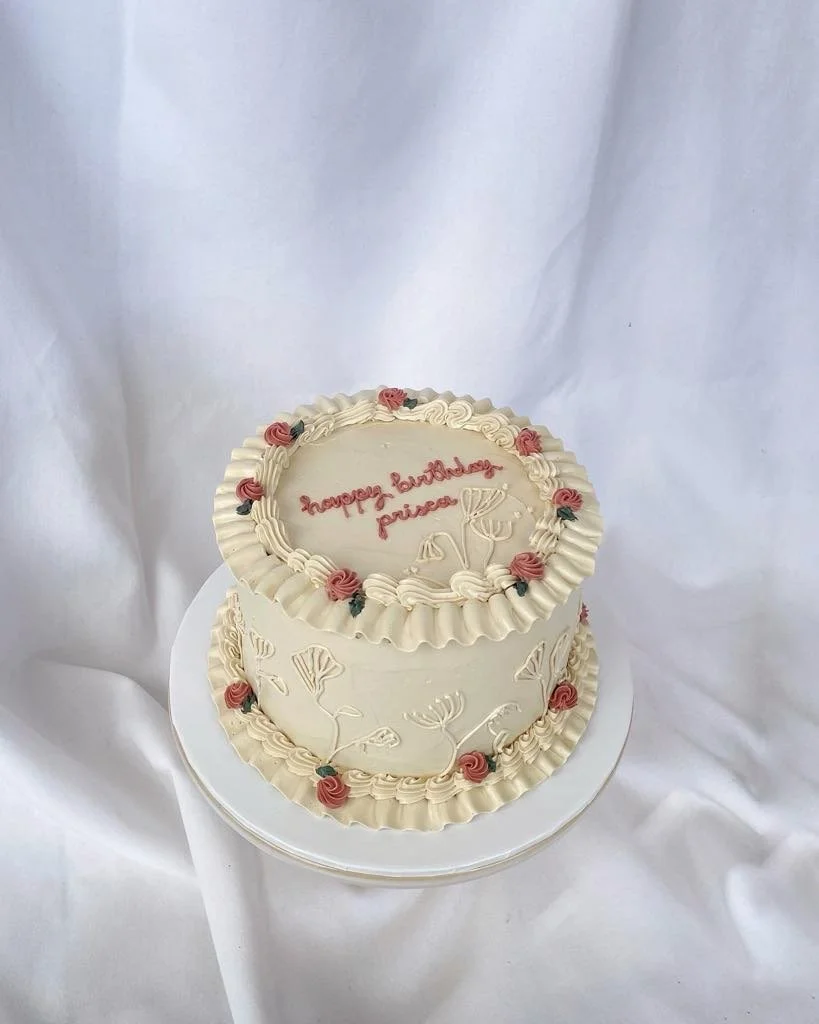Two-tiered cake decorated with floral icing, with a message written in pink icing that says "Happy Landings, Princess".