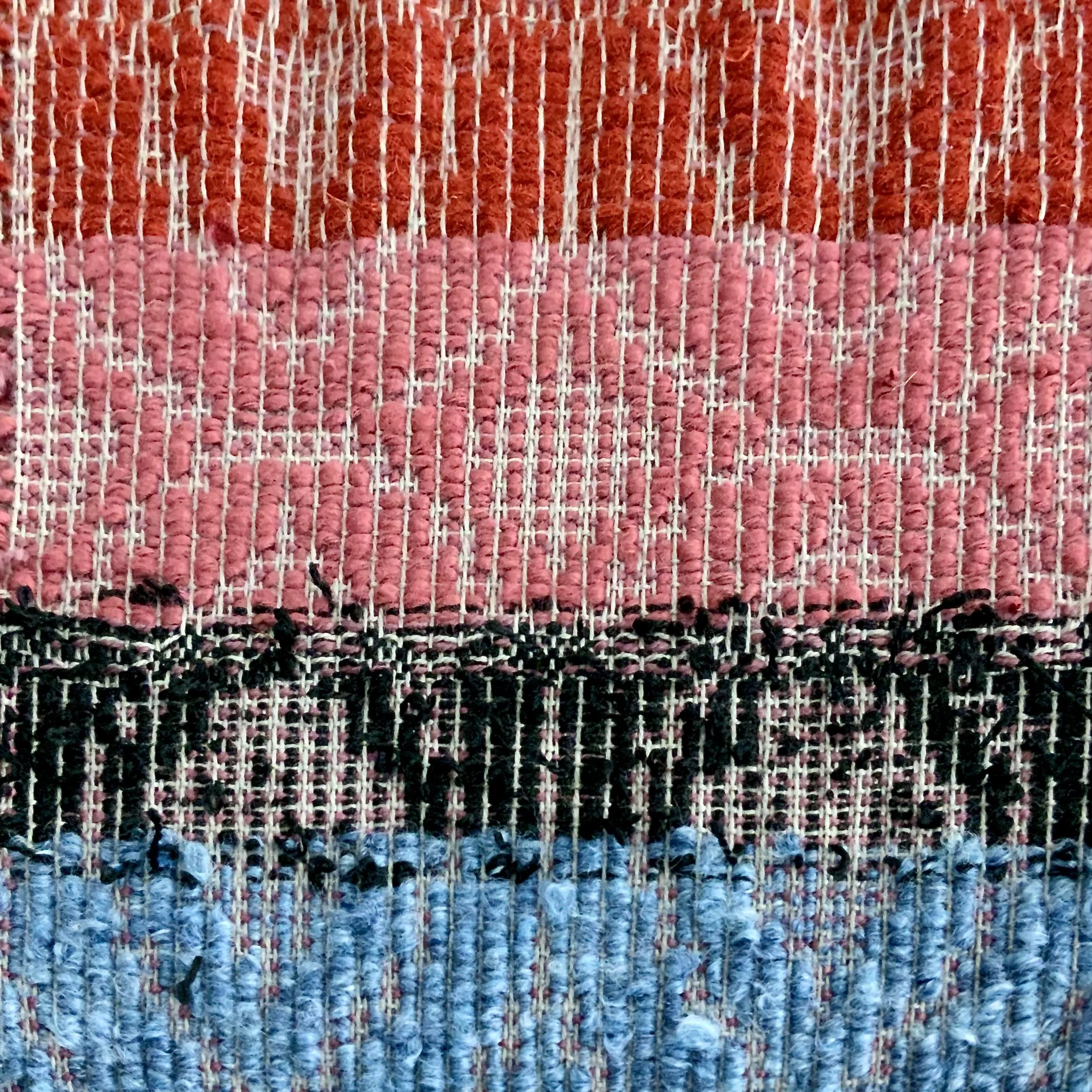 Close-up of a woven textile with horizontal color stripes in orange, pink, black, and blue.
