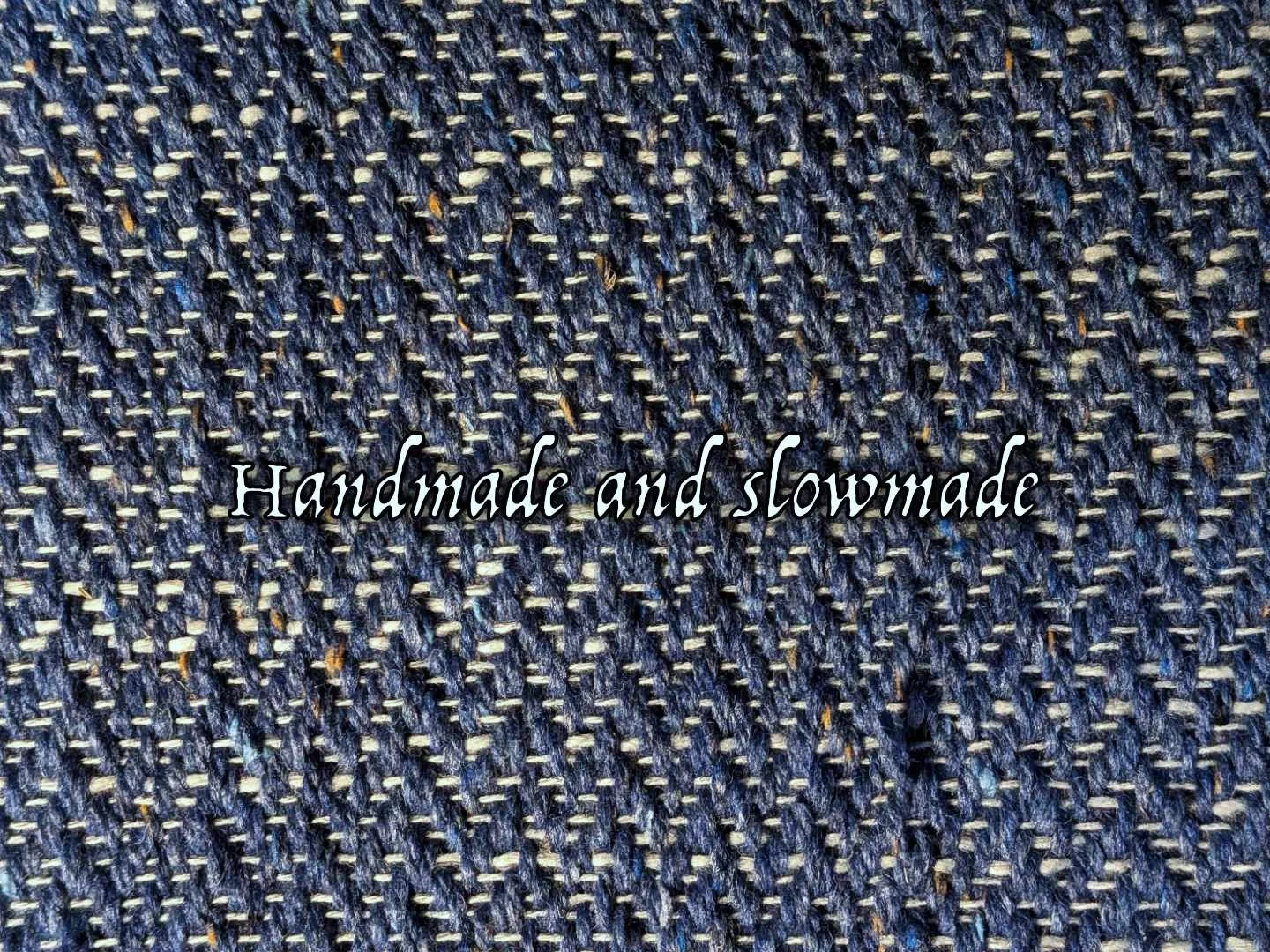 Close-up of dark blue woven fabric with the words 'Handmade and slowmade' overlaid.
