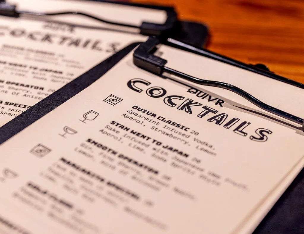 Close-up of a cocktail menu on a clipboard with a wooden table in the background.