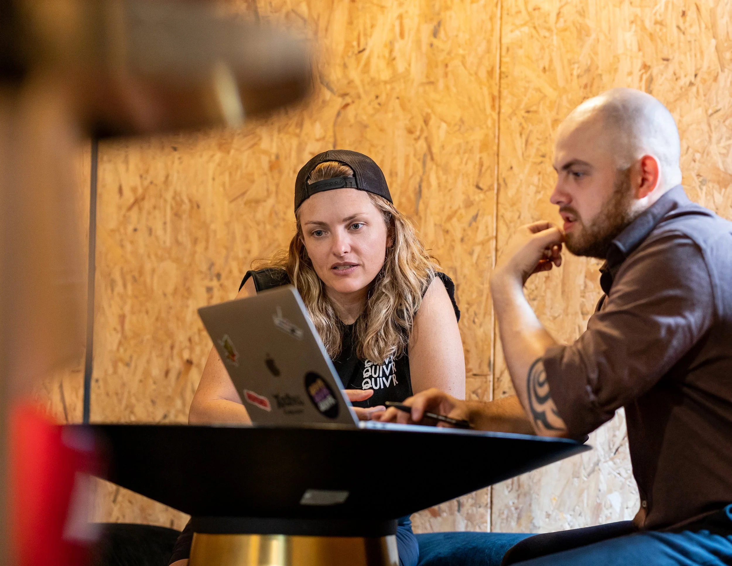 Two people, a woman and a man, sitting at a small black table, looking at a laptop in a room with wooden walls. Talking to the consultancy services that Greenpoint Hospitality offer.