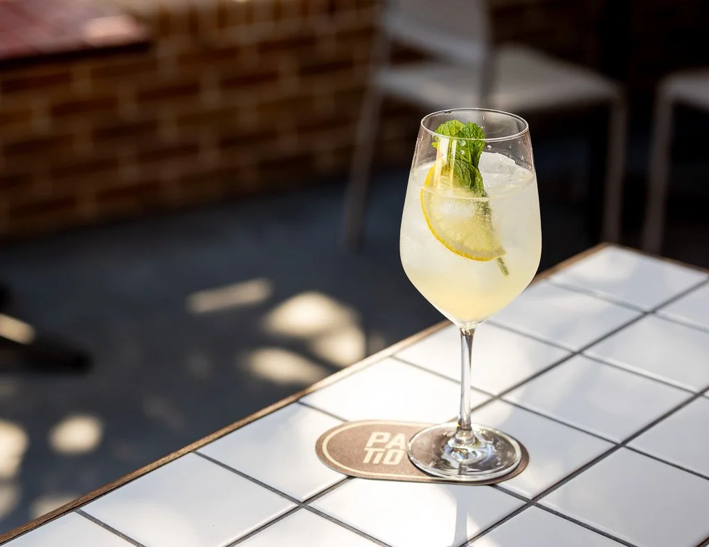 A glass of lemonade with lemon slices and mint leaves on a white tiled table outdoors.