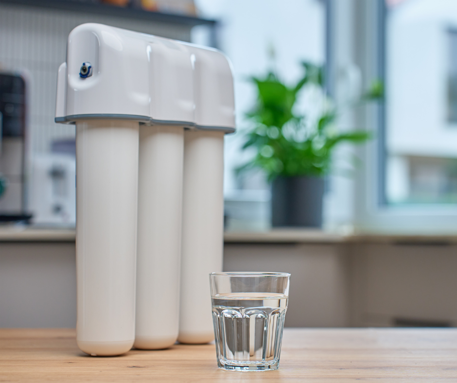 A water filtration system and a glass of water on a wooden table in a kitchen.