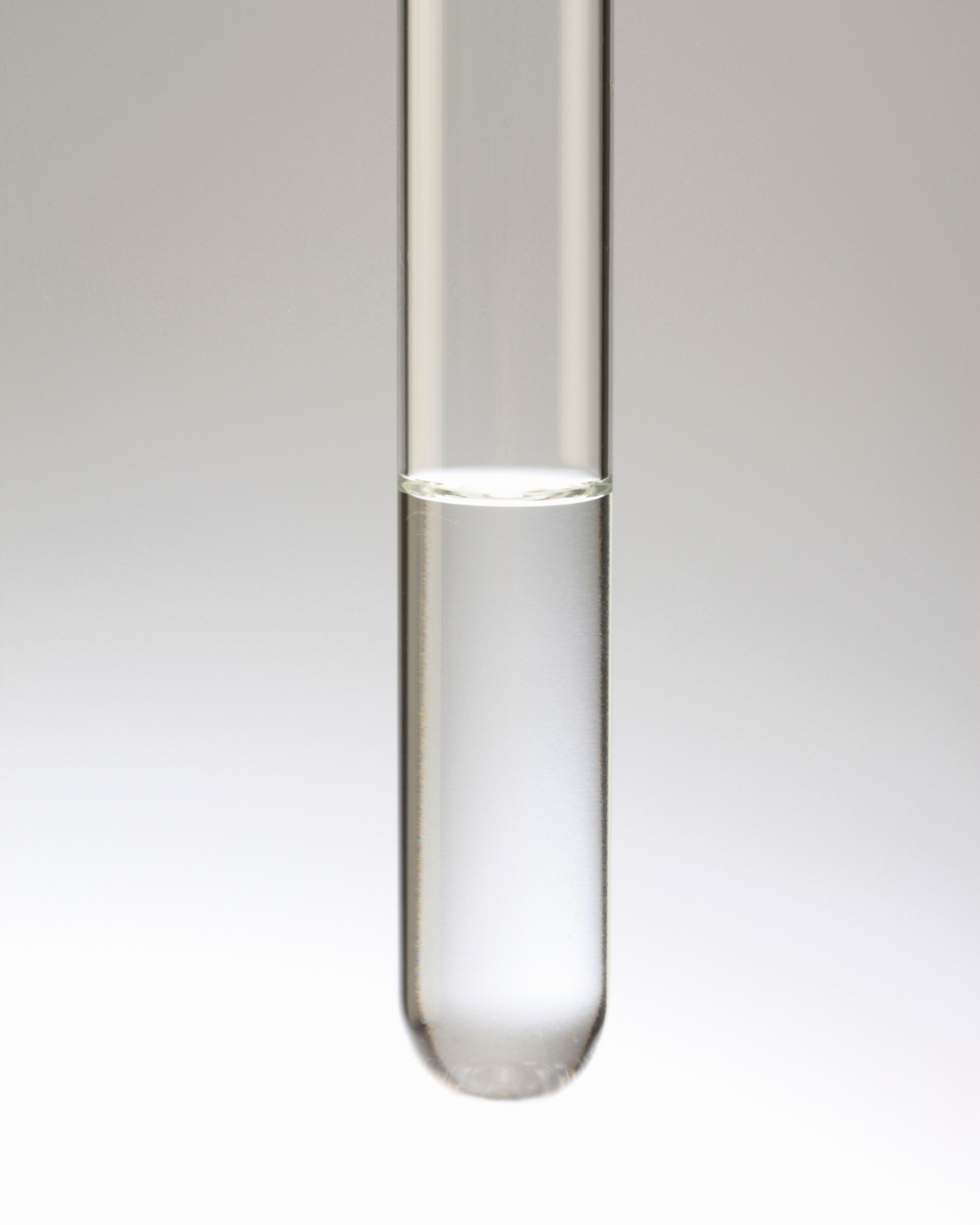 Close-up of a clear glass test tube filled with transparent liquid against a plain background.