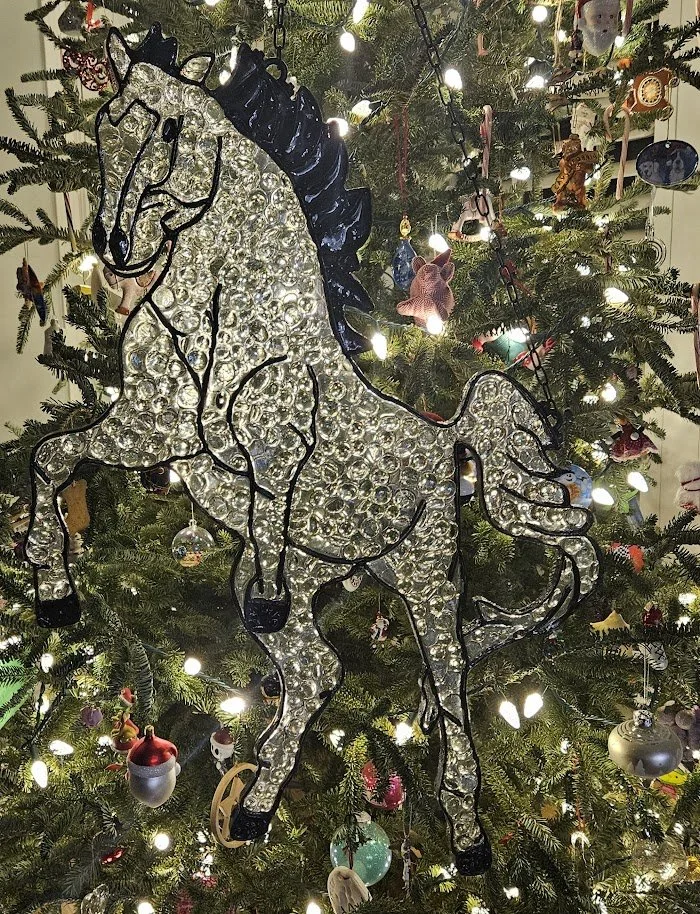 A Christmas tree decorated with various ornaments and lights, featuring a large, illuminated horse-shaped ornament in the foreground.