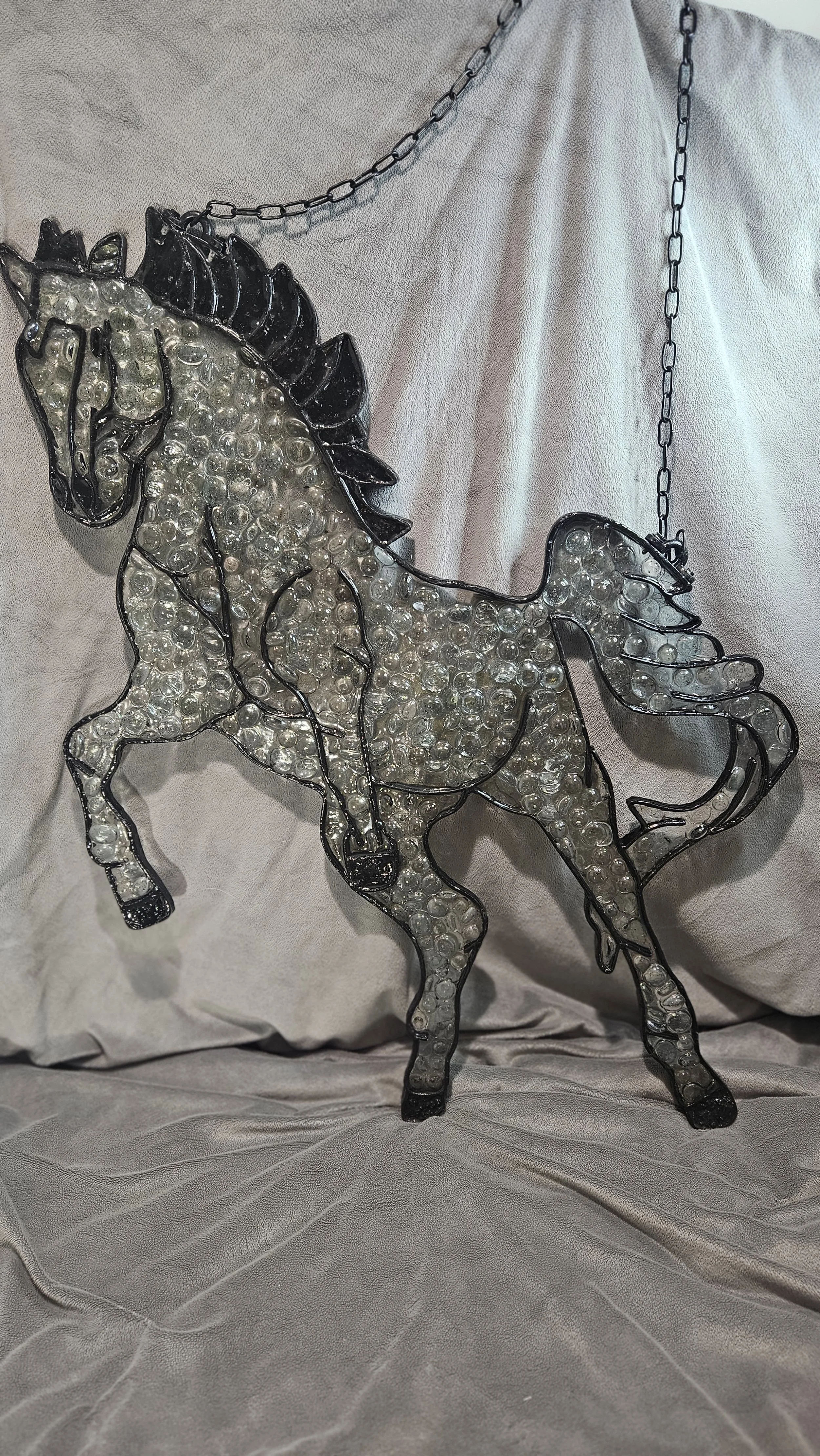 Decorative white and black horse figurine with pearl accents, hanging from a chain, displayed in front of a light-colored fabric backdrop.