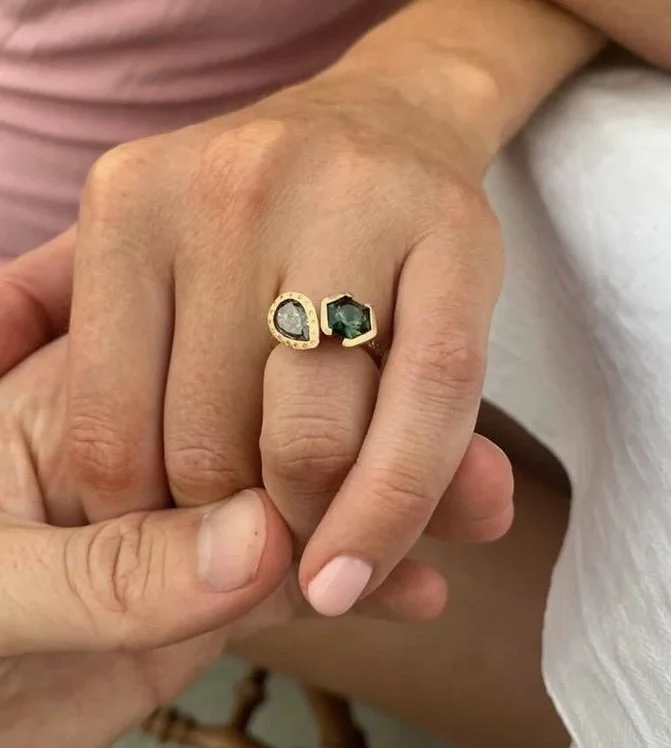 Close-up of a hand with two rings, one with a clear stone and the other with a dark green stone.