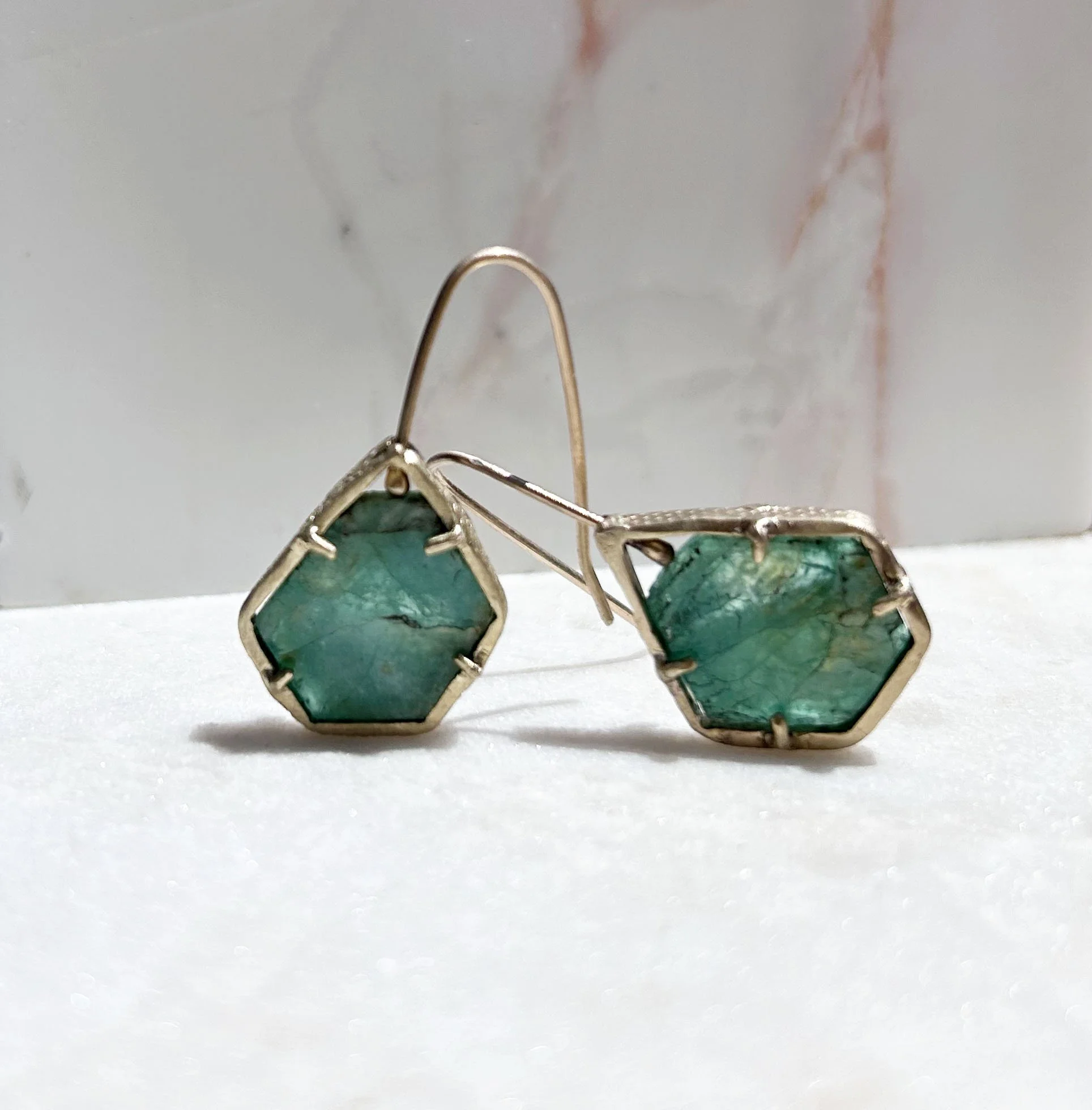 Silver earrings with hexagonal green gemstones on a white surface with a marble background.
