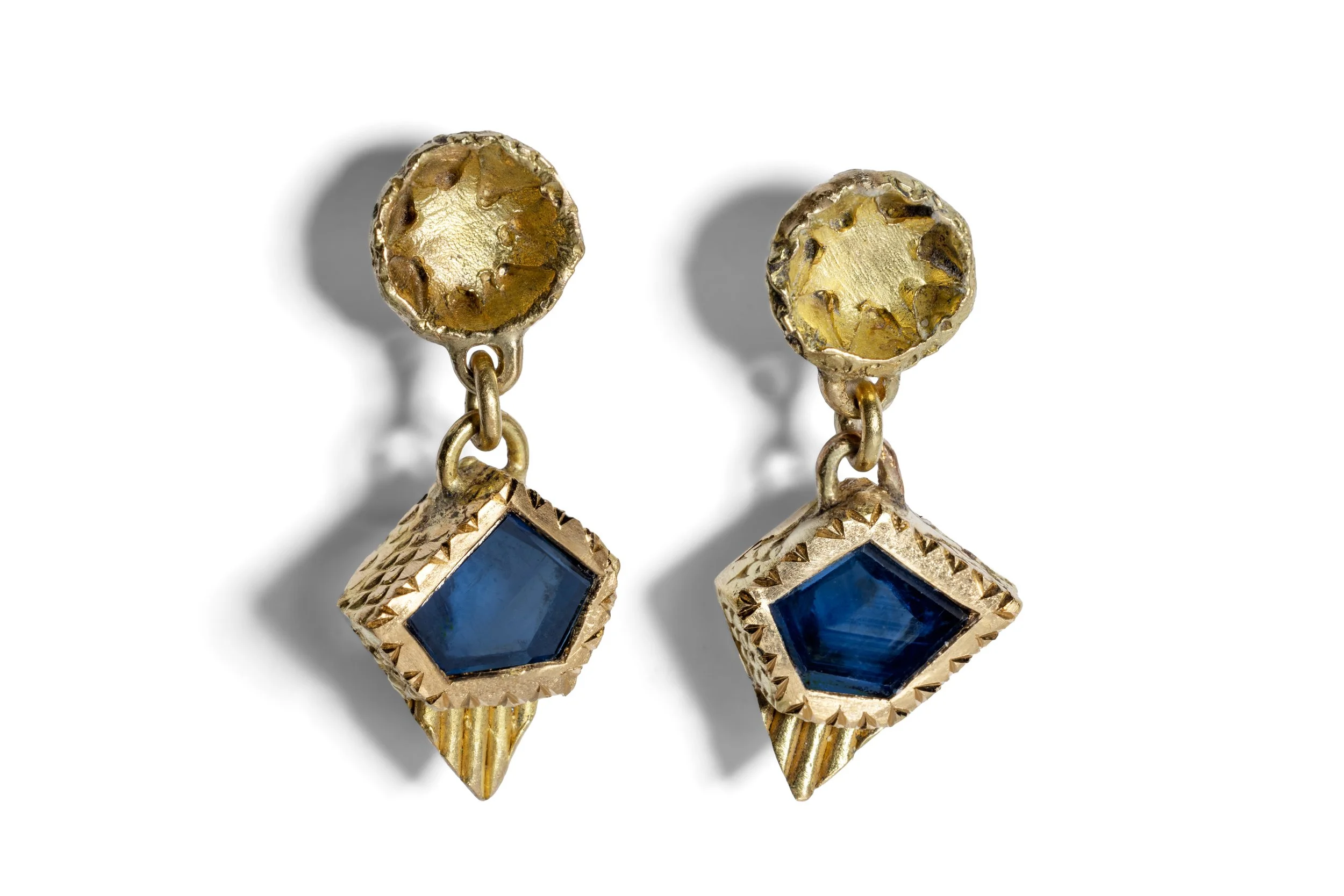 A pair of gold earrings with blue gemstones hanging from circular gold studs against a white background.