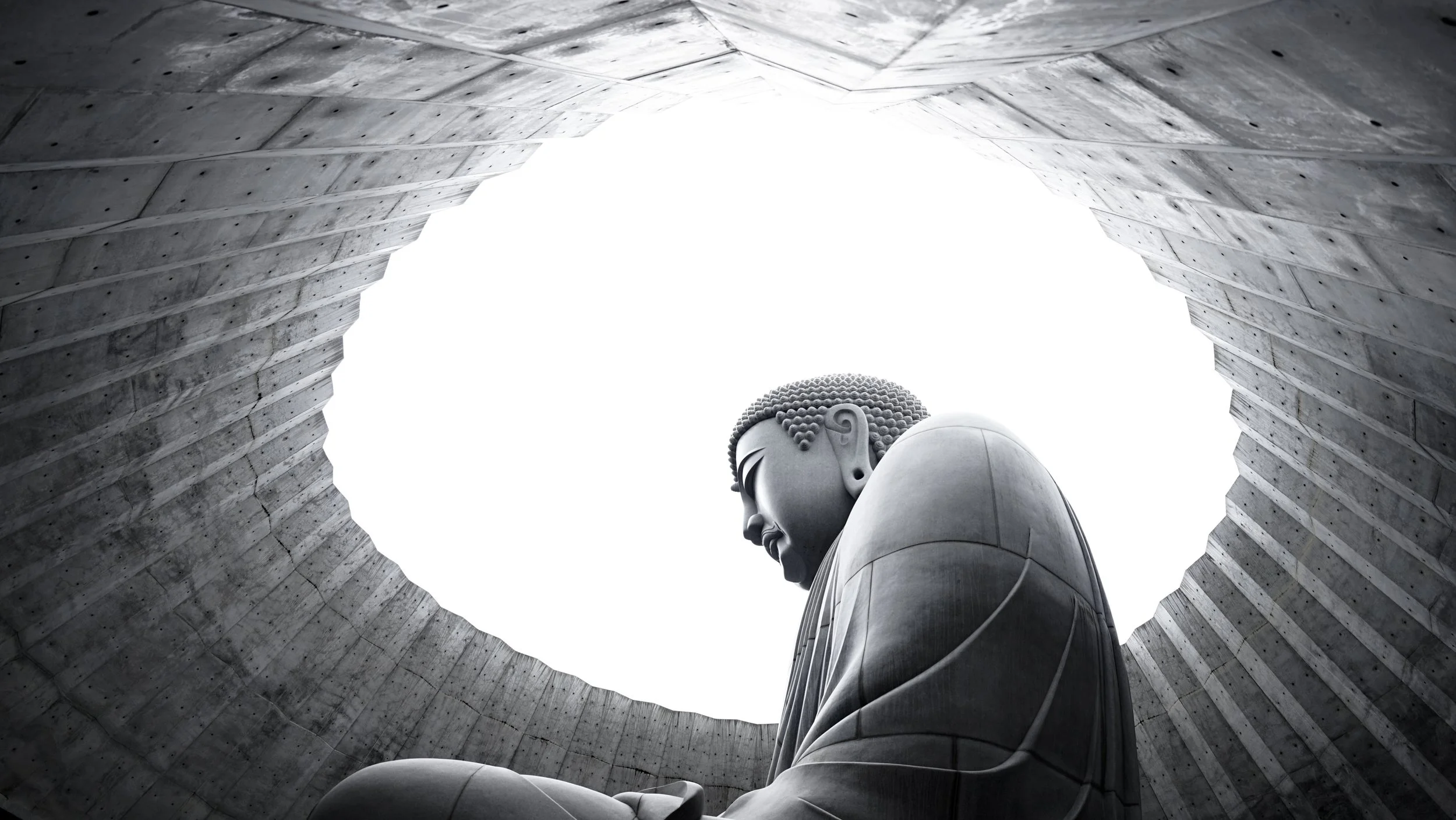 A large Buddha statue viewed from below, seen through a circular opening in a concrete structure with angular walls.