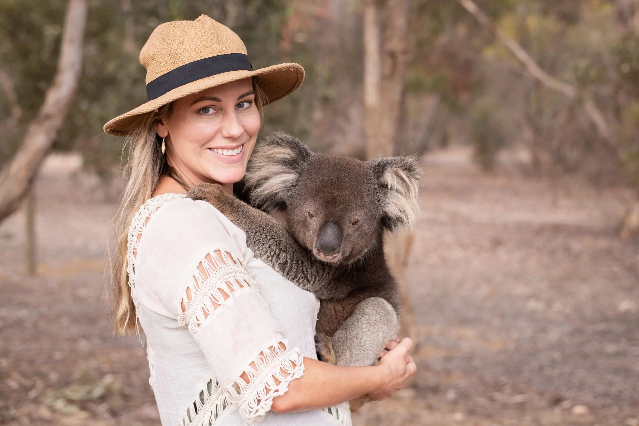 A woman wearing a wide-brimmed sun hat and earrings, smiling while holding a koala at the Kangaroo Island Wildlife Park.