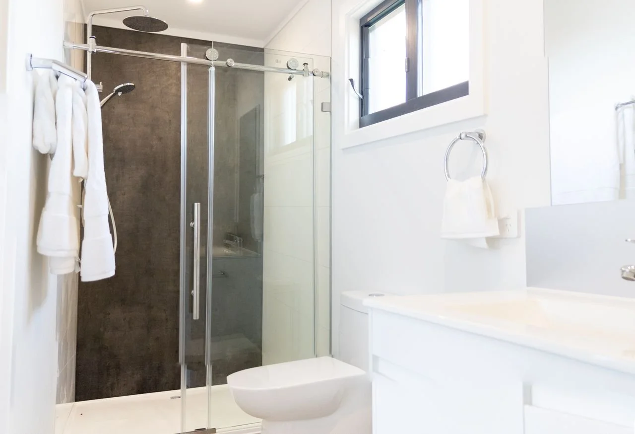 Modern bathroom with white walls, a glass shower enclosure, a window, a toilet, and a sink.