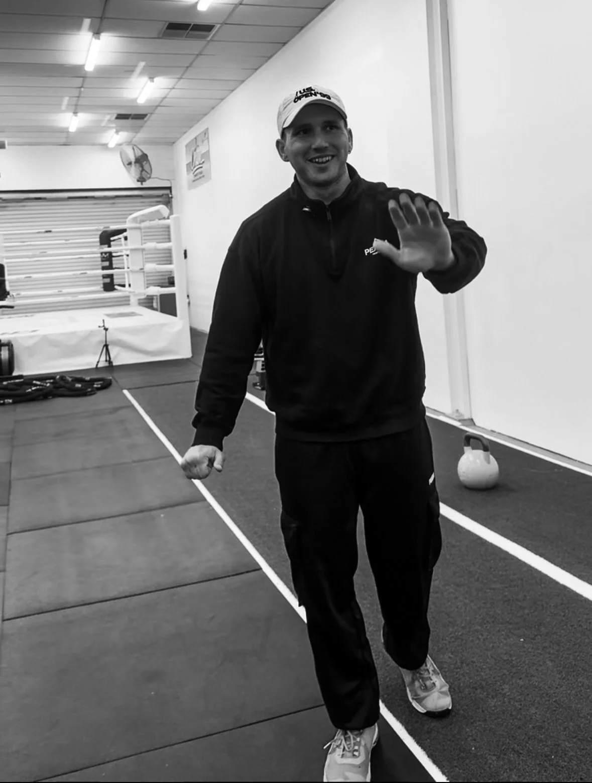 Personal trainer smiling and waving inside a gym, ready to coach strength and performance sessions