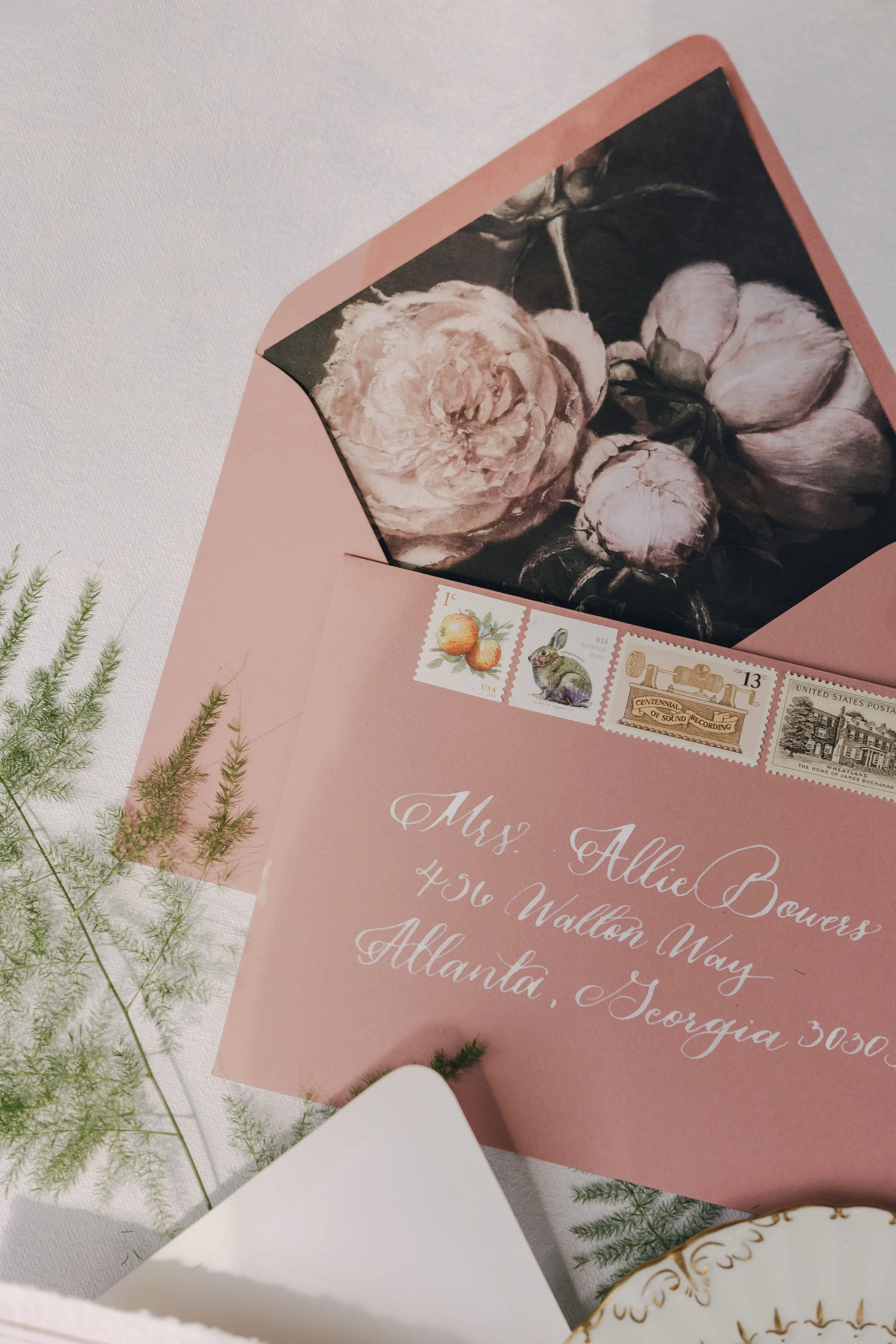 Pink envelope addressed to Mrs. Allie Bowers in Atlanta, Georgia, with vintage postage stamps including oranges, a rabbit, and historical landmarks. Inside the envelope is a black and white floral painting of peonies.