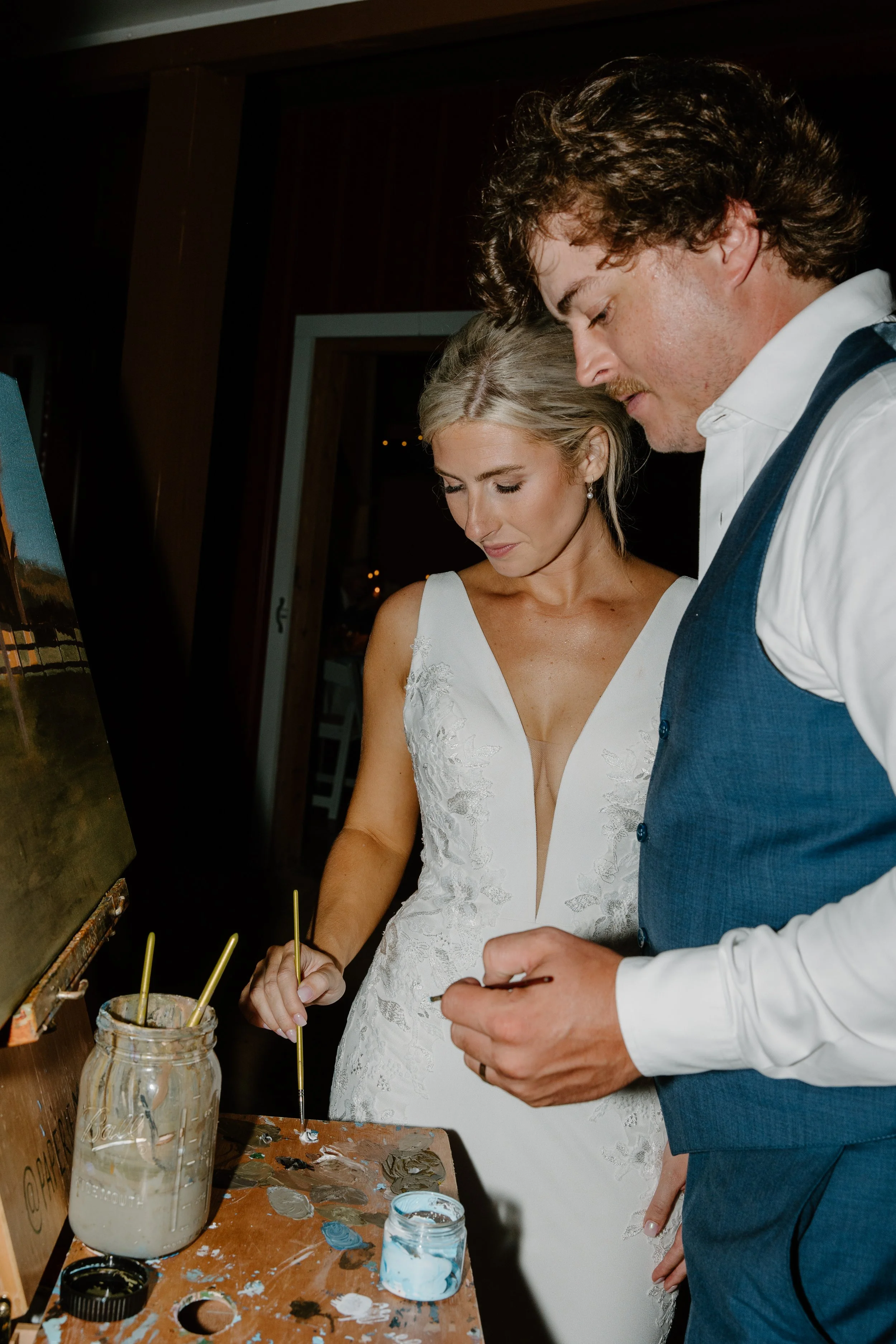 A bride and groom painting on a canvas together at a wedding reception.