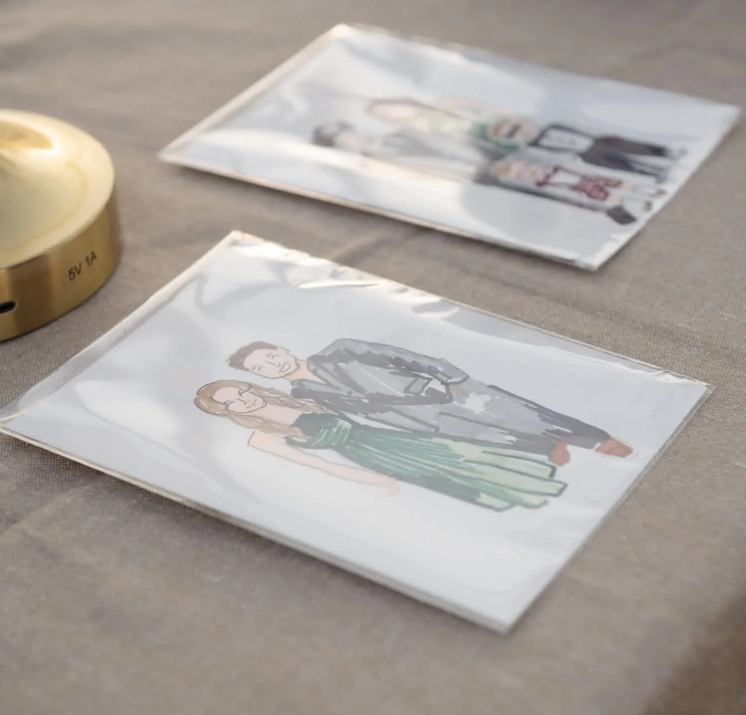 Colorful illustrated paper dolls of a male and female standing side by side on a beige table, with a small lamp nearby.