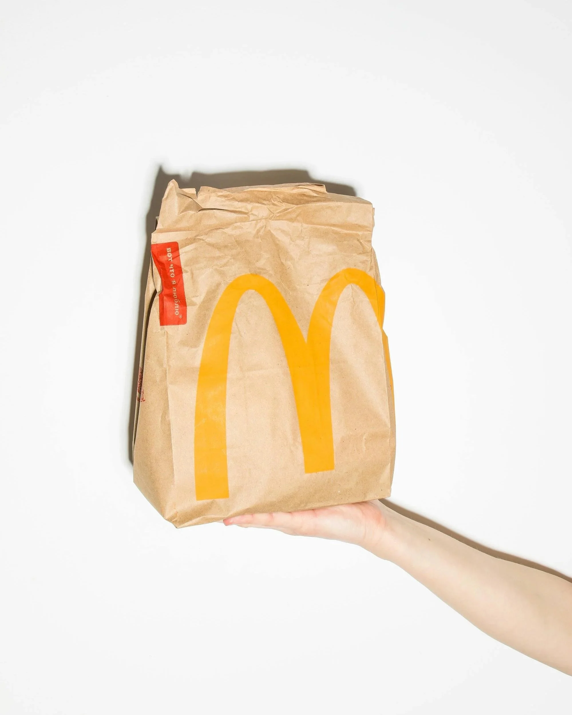 A hand holding a McDonald's paper bag with the golden arches logo, against a white background.