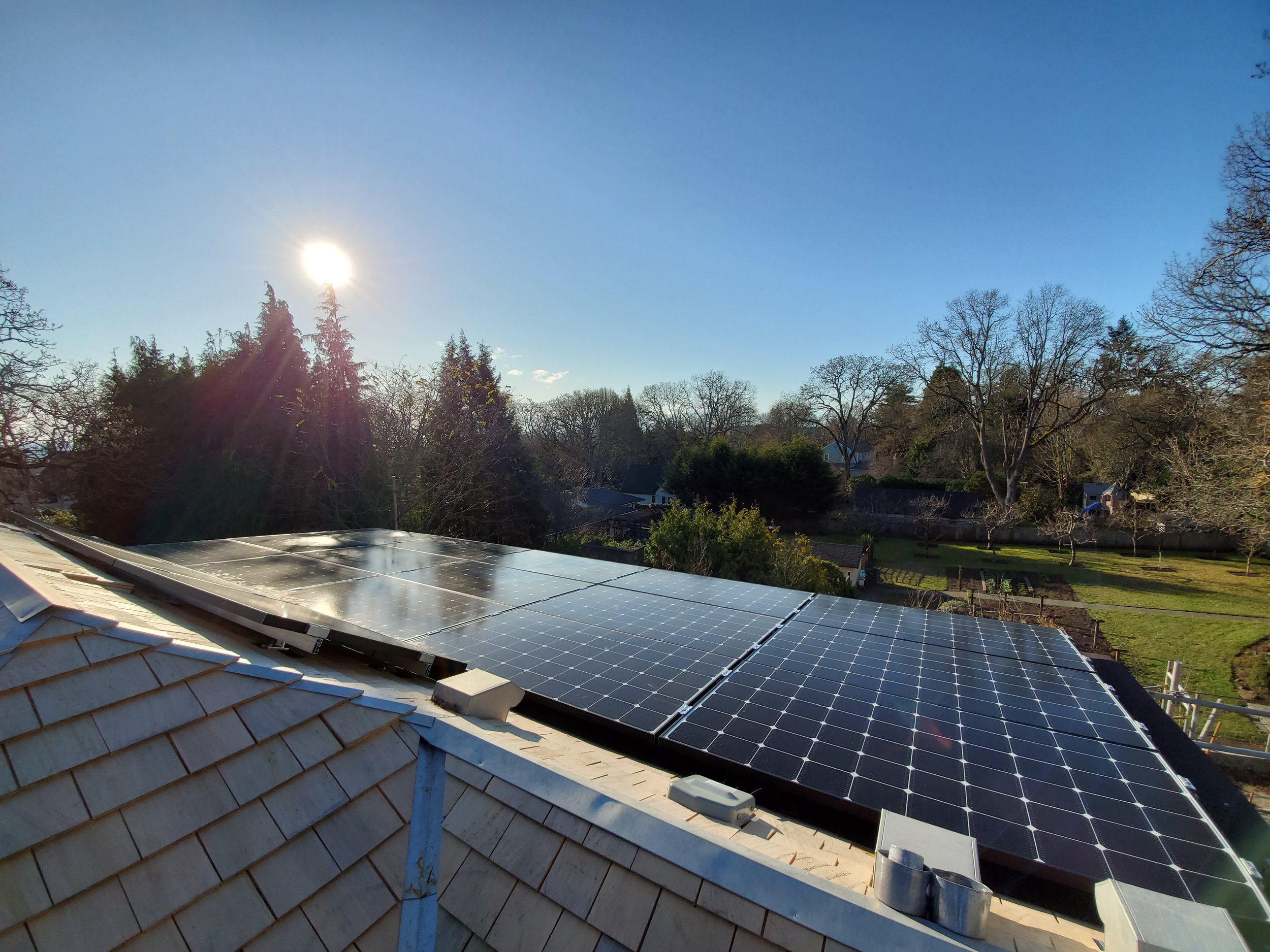 Solar panels installed on a residential roof under a clear blue sky with the sun shining.