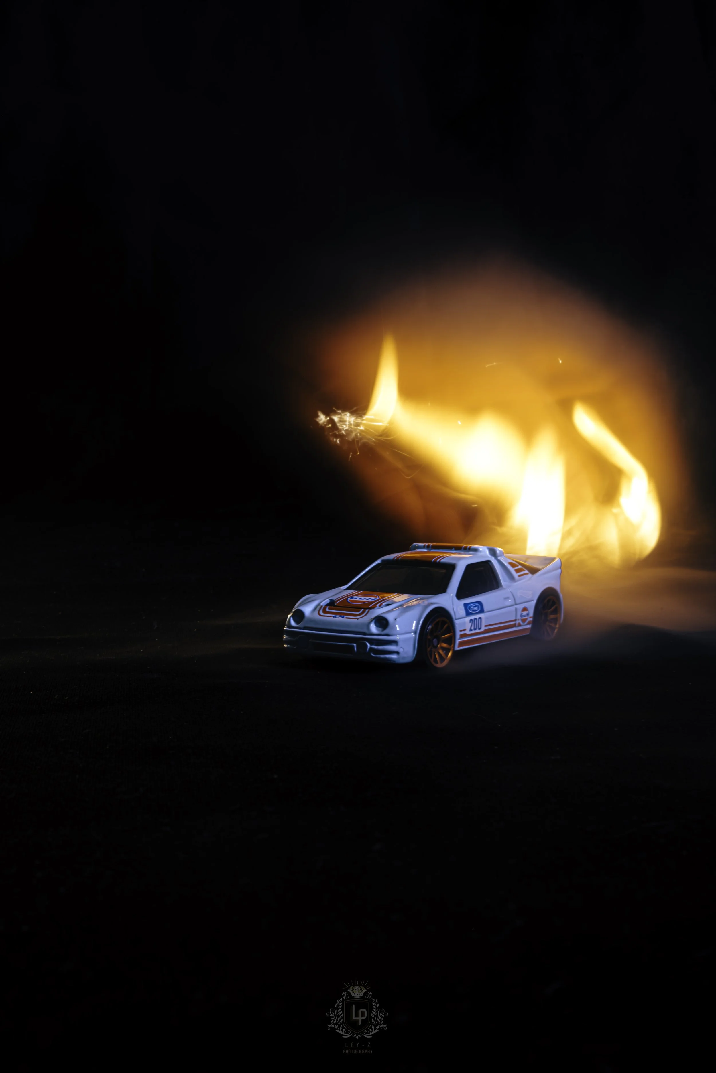 A toy race car with racing decals on a dark background, engulfed in flames.