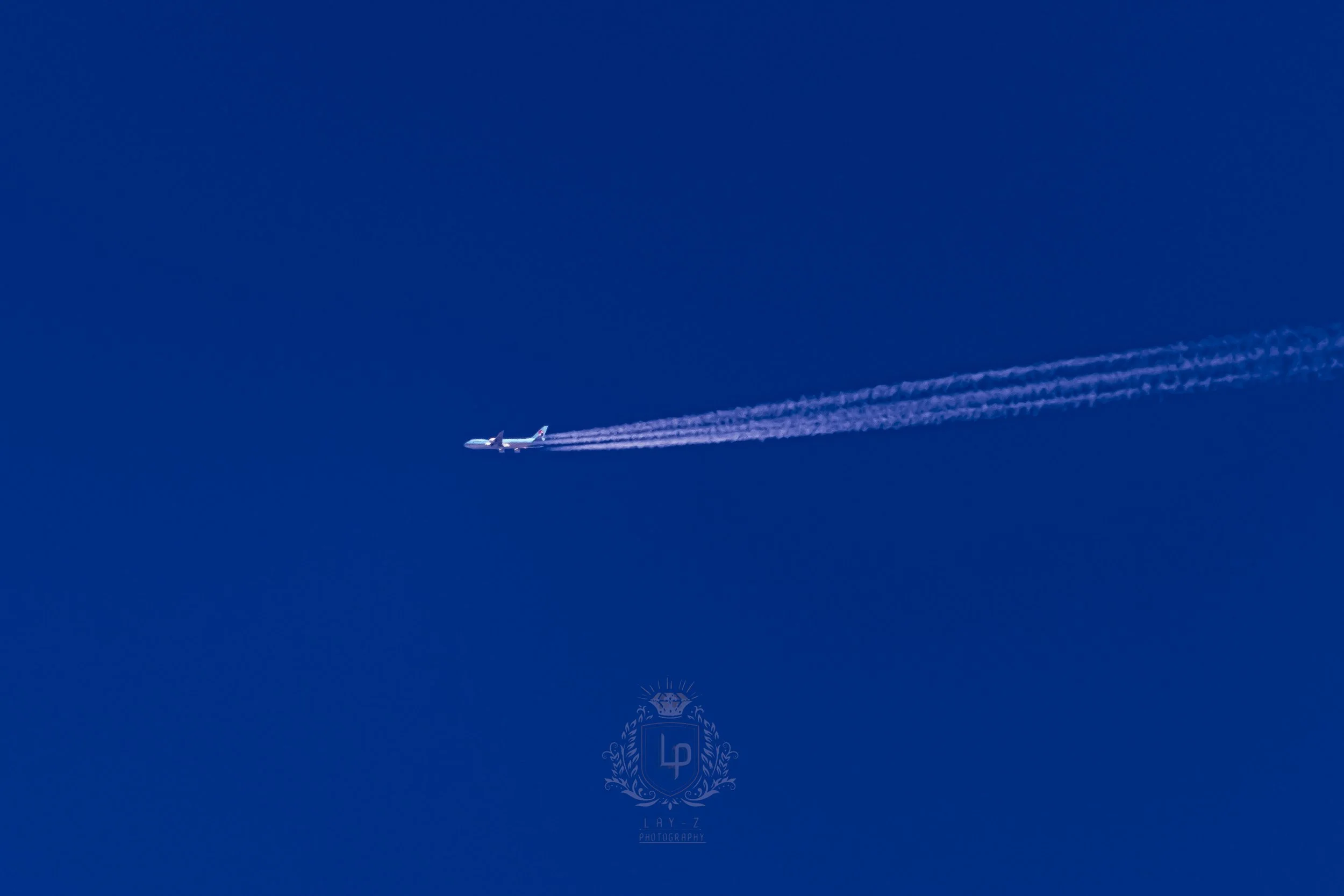 Airplane flying in a clear blue sky leaving white contrails behind.