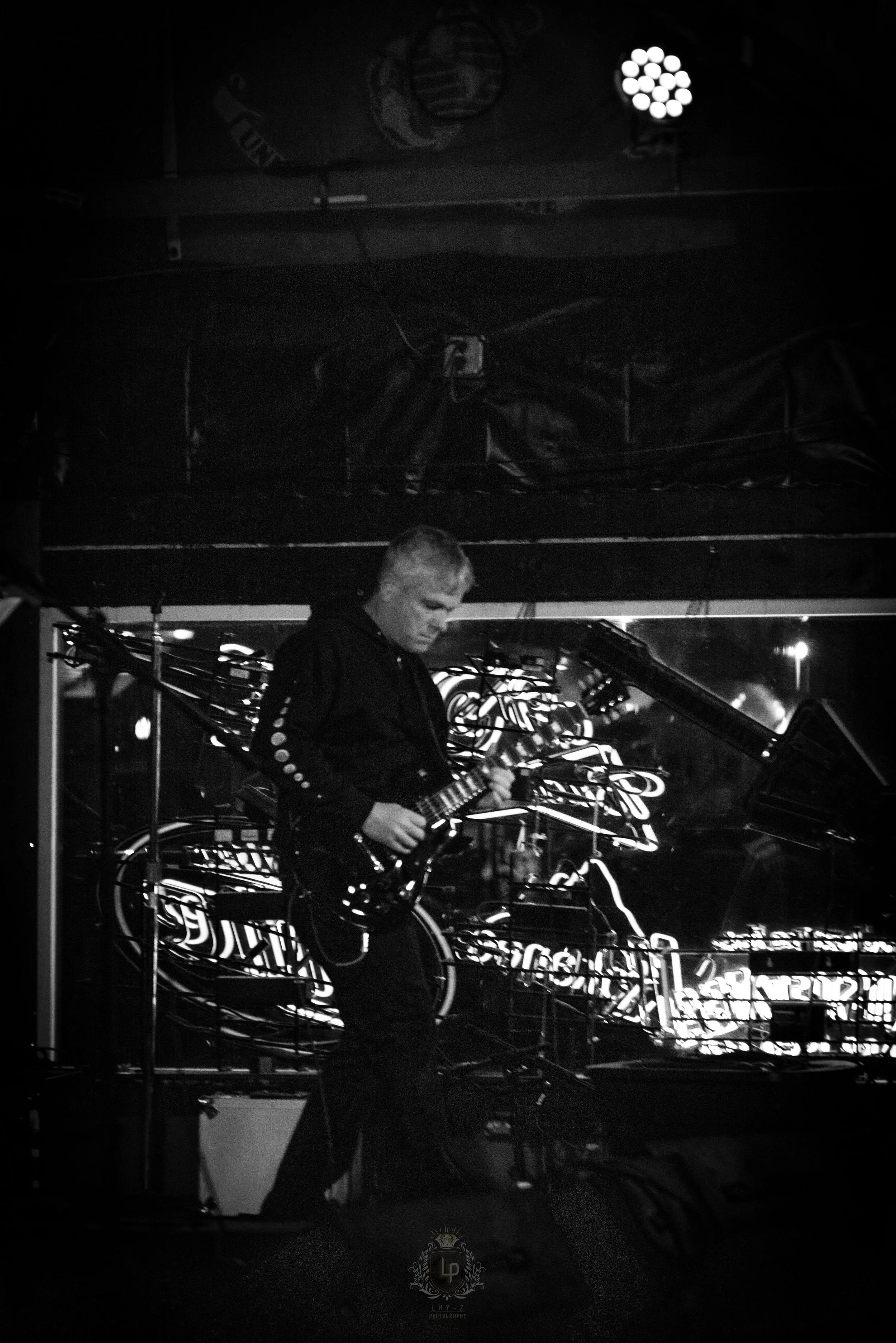 A person playing an electric guitar on stage at night, with neon signs and stage lights in the background.