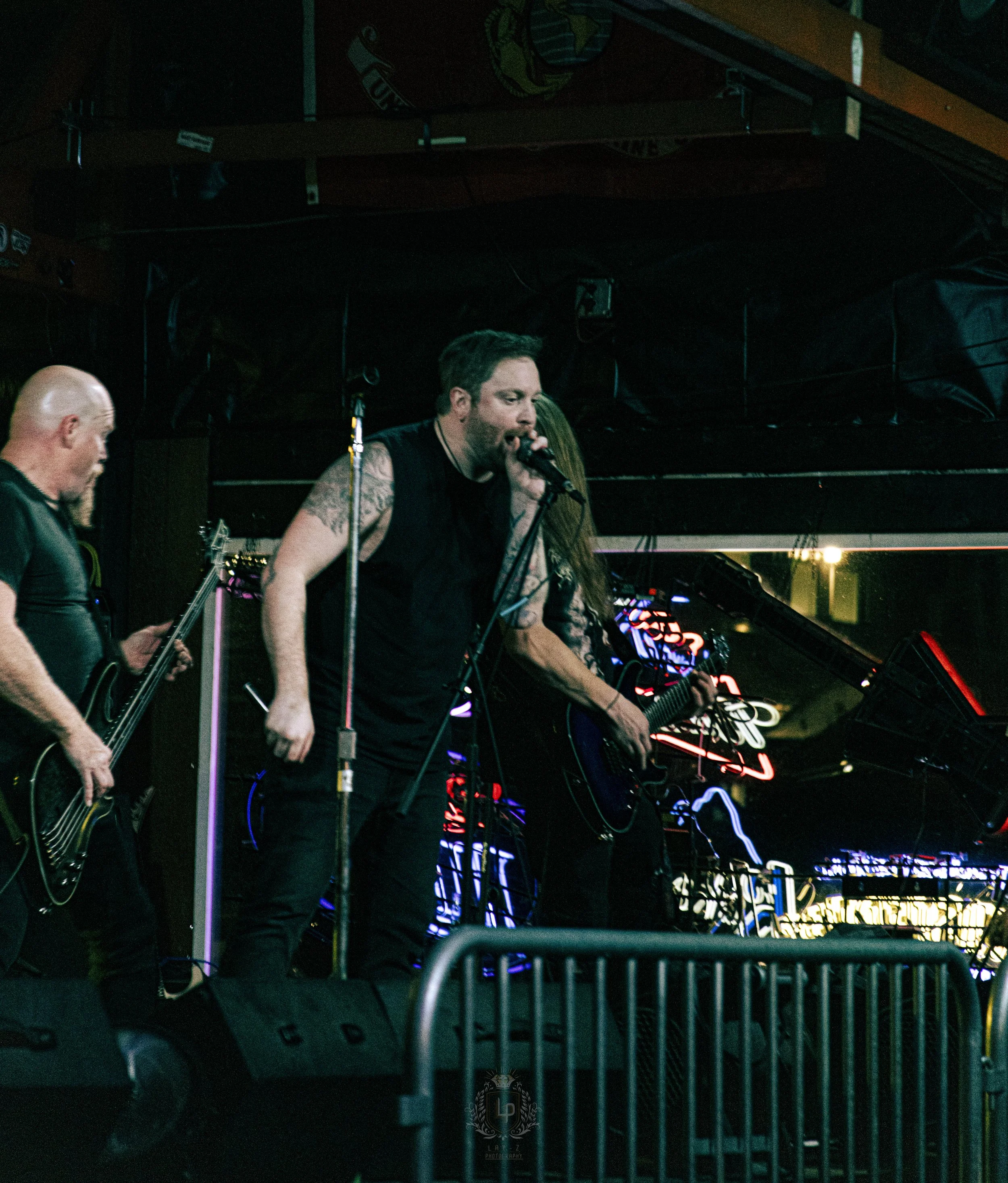 Band performing live on stage in a dimly lit venue, with neon signs in the background.