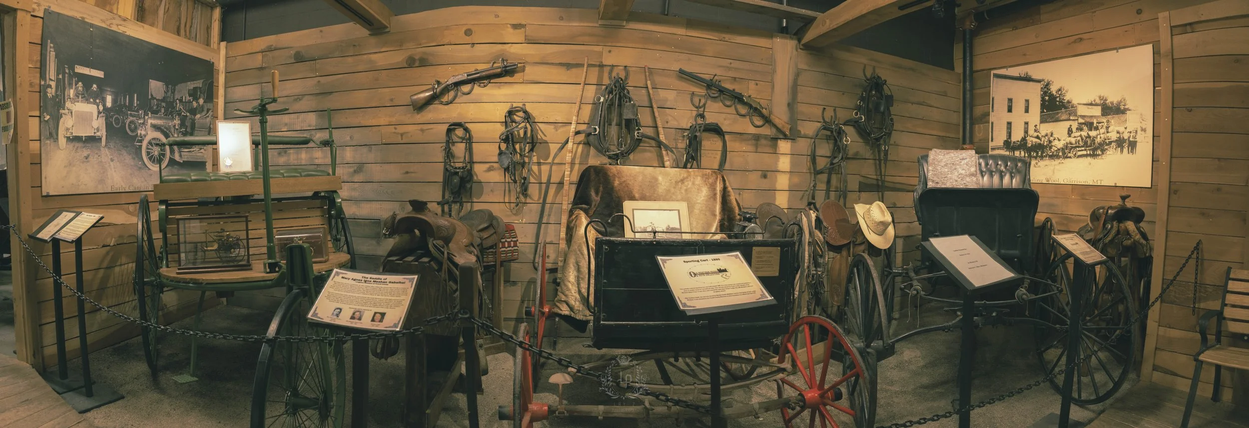Historical display of vintage carriages and harnesses in a museum with informational plaques and black-and-white photographs on wooden walls.