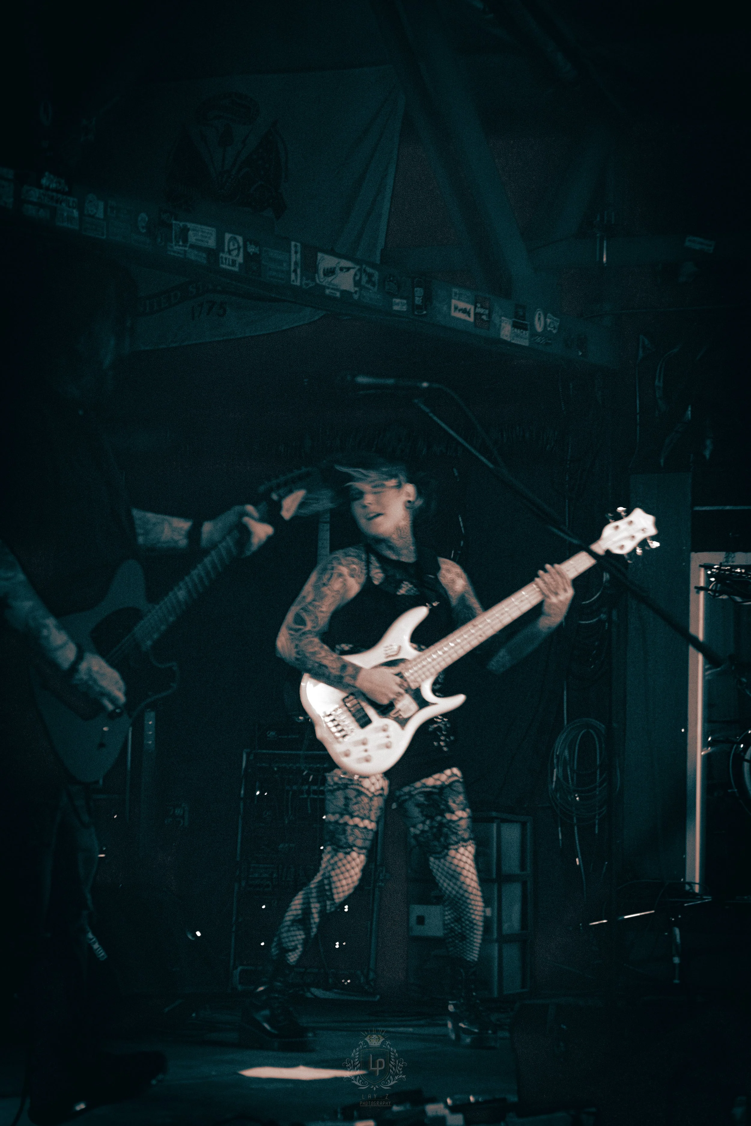 Female musician with tattoos playing a white bass guitar on stage in a dark venue.