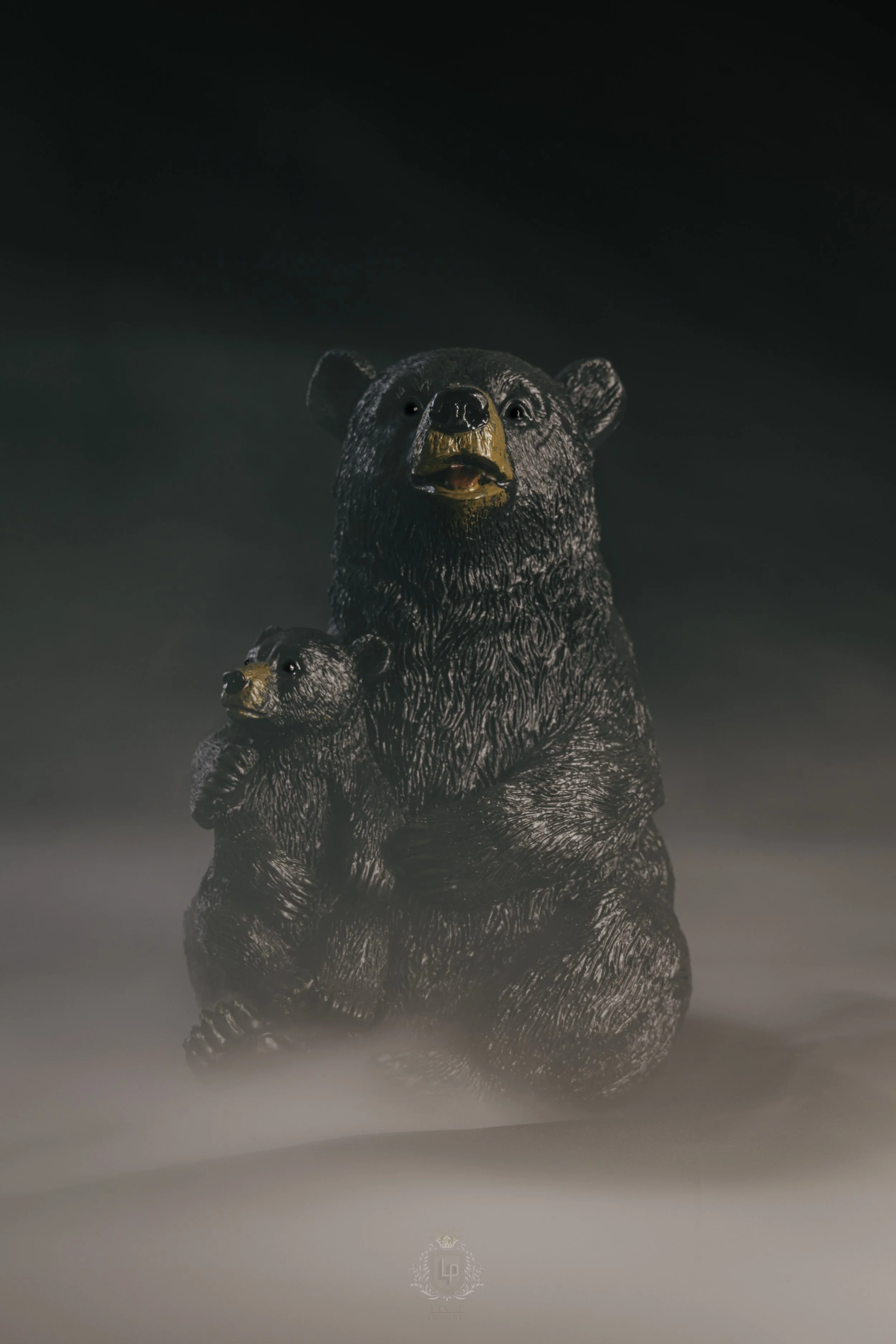 A statue of a bear with a cub, both made of dark material, set against a dark sky with fog or mist at the base.