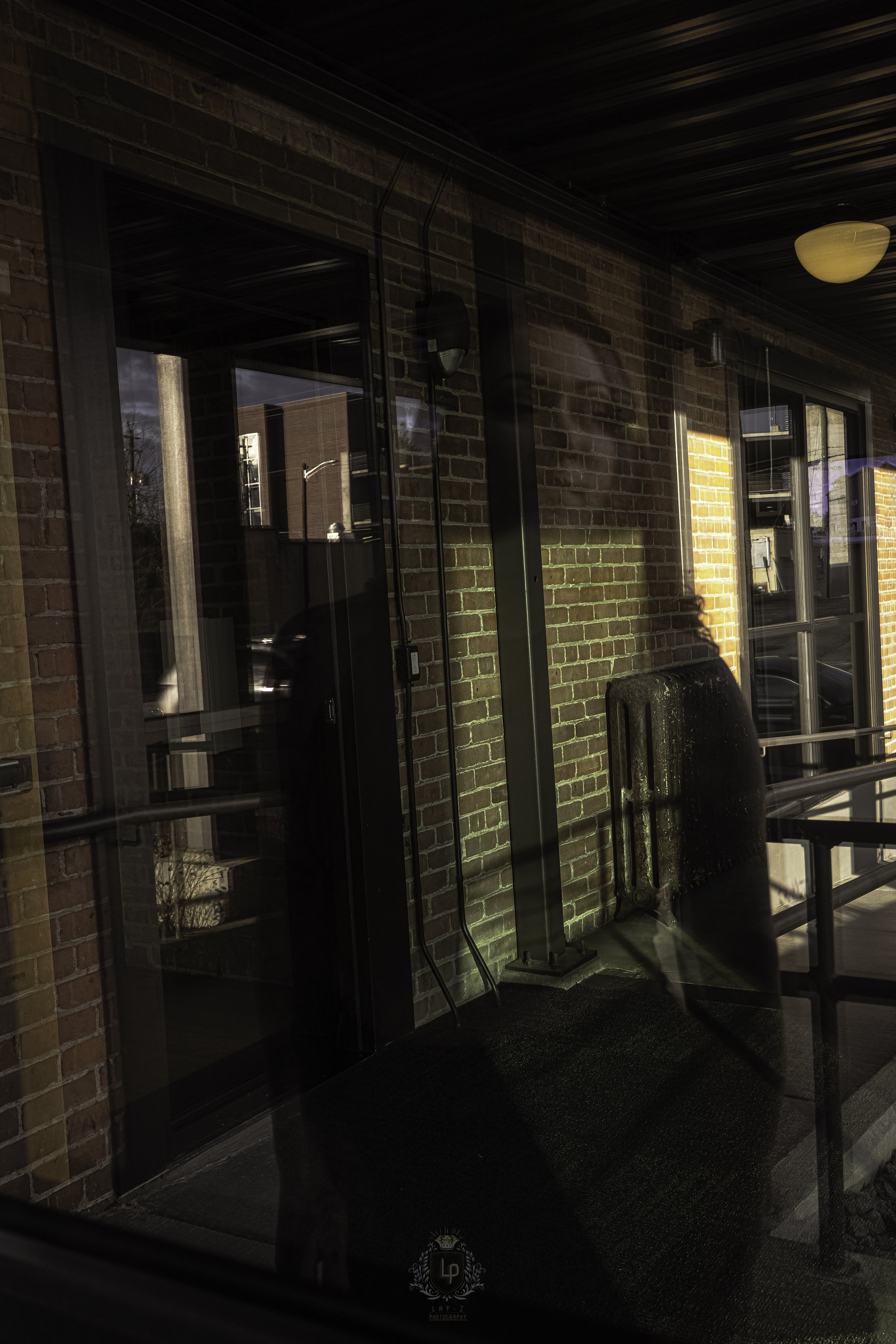 Reflective glass window showing a person and buildings on a brick wall balcony with a black metal railing.