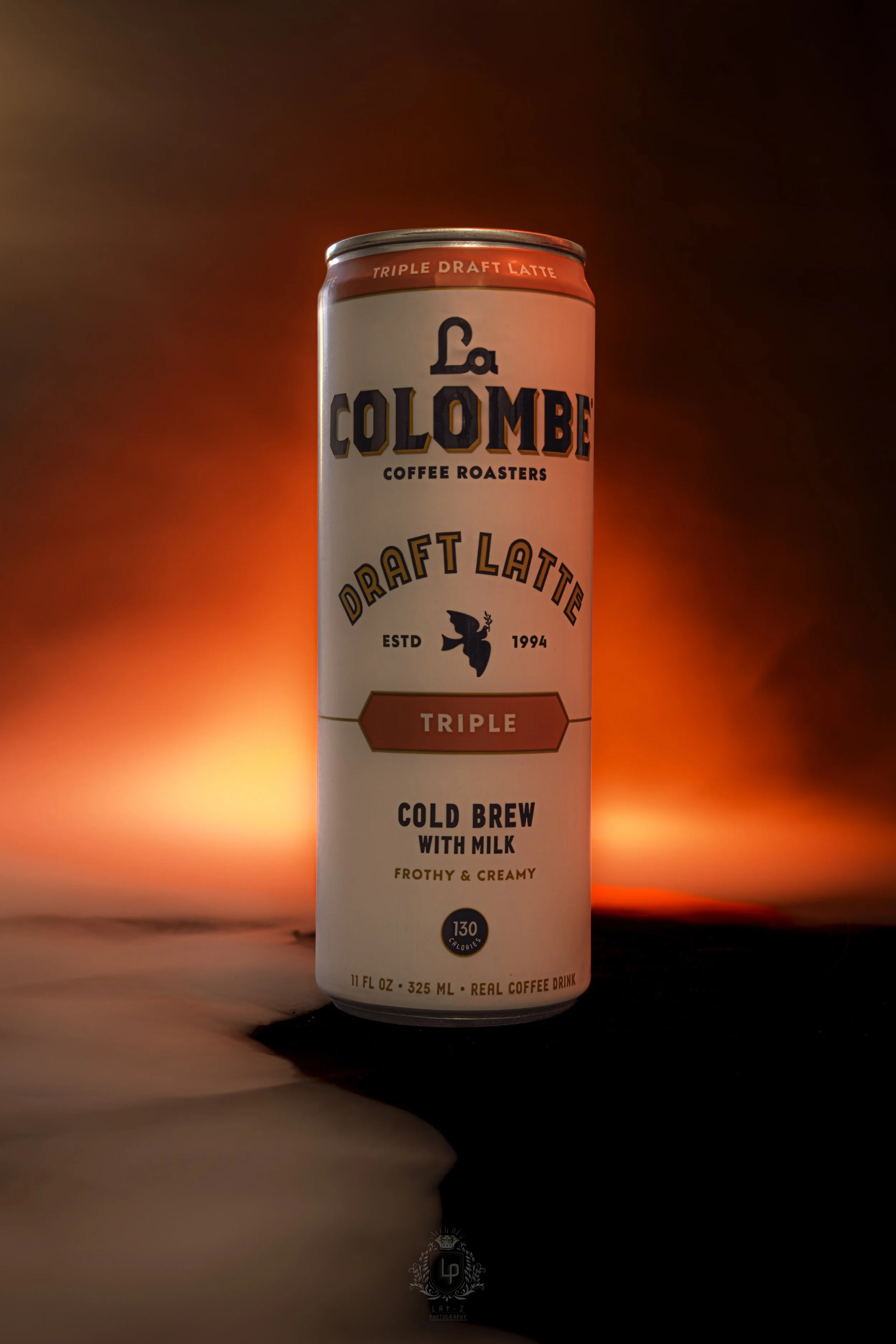 A tall can of La Colombe Draft Latte Triple flavor cold brew with milk, frothy and creamy, standing against a blurred red and dark background.