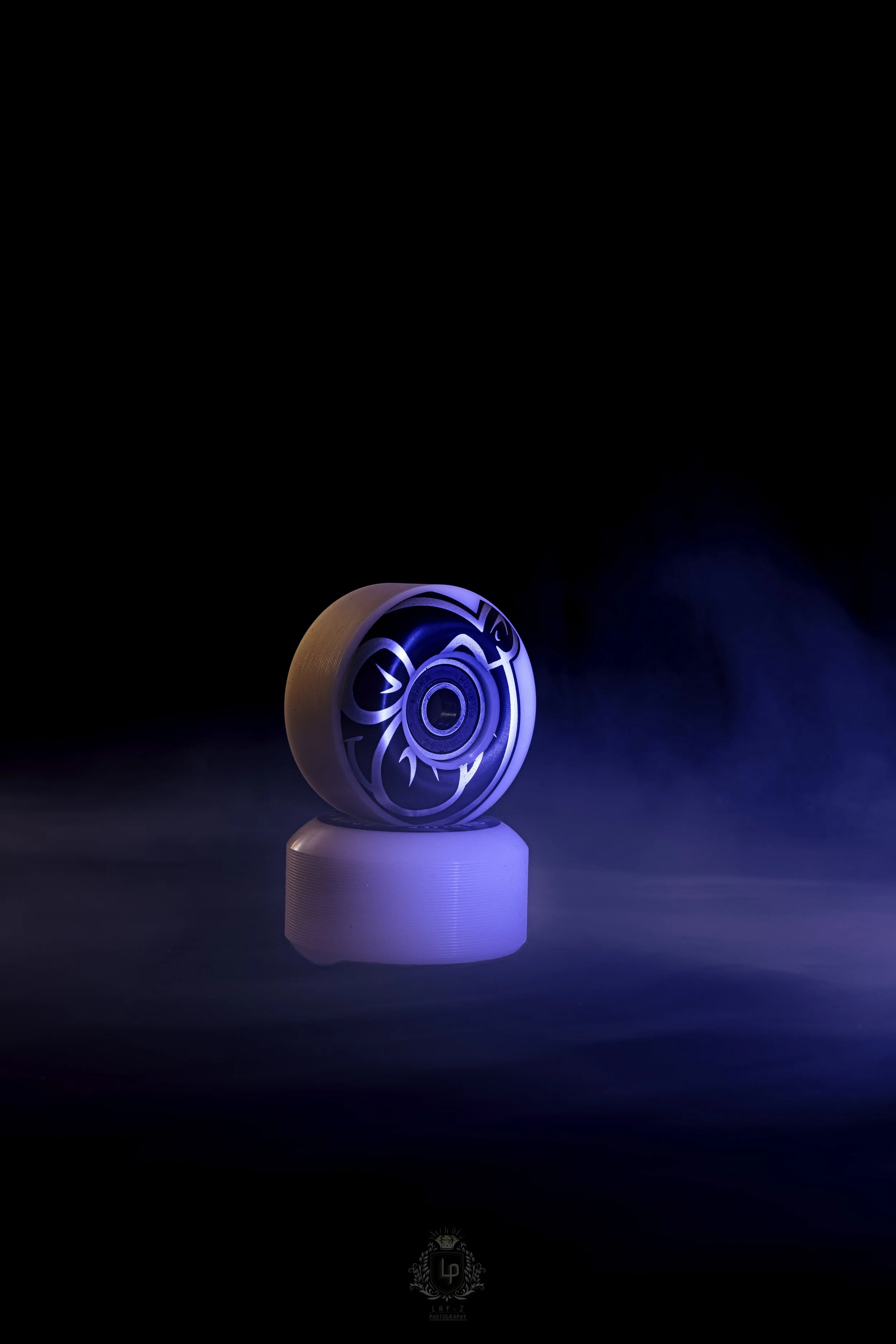 A skateboard wheel illuminated with blue light, sitting on a white skateboard riser against a dark background.