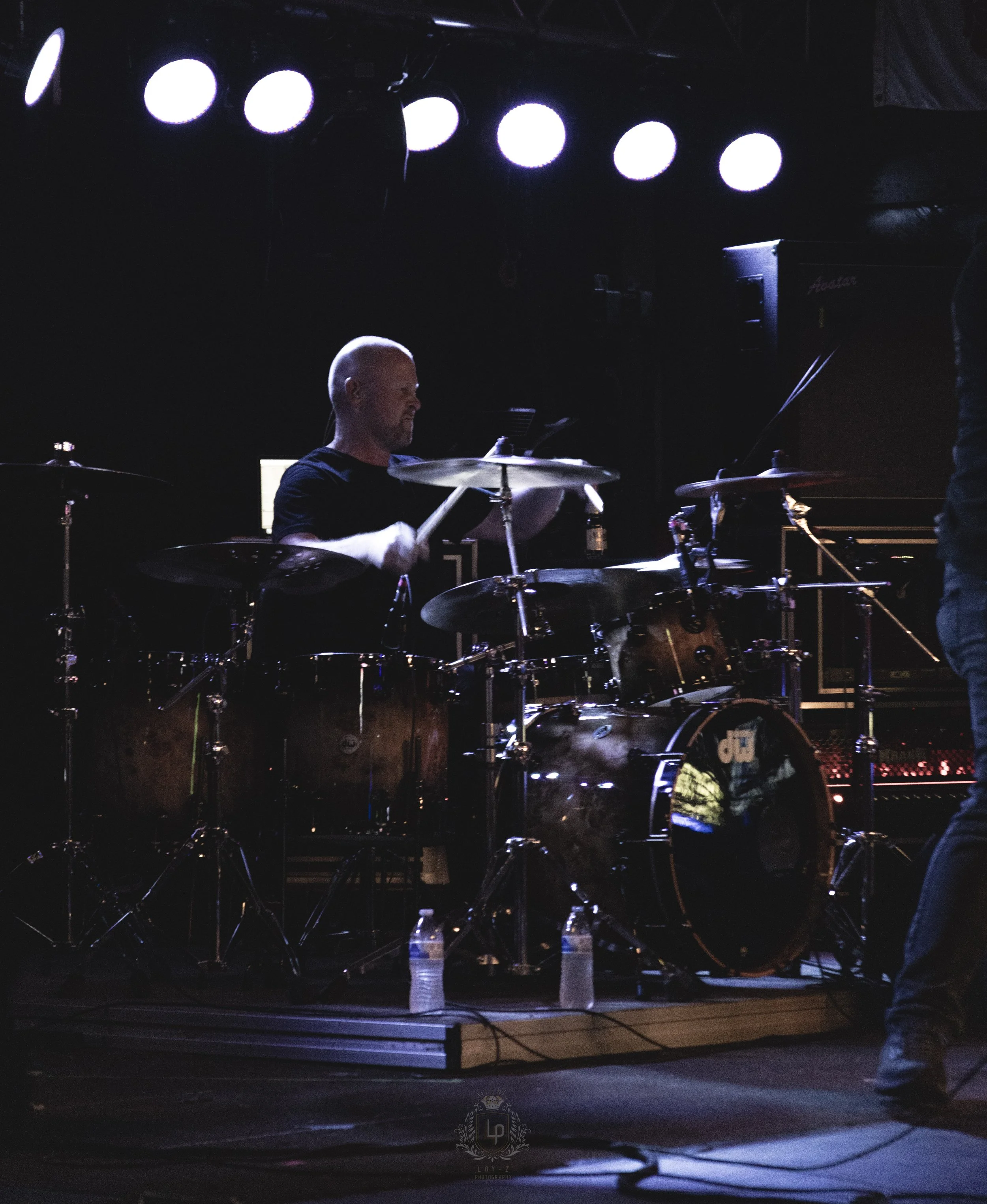 Bald man playing drums on stage with bright lights overhead