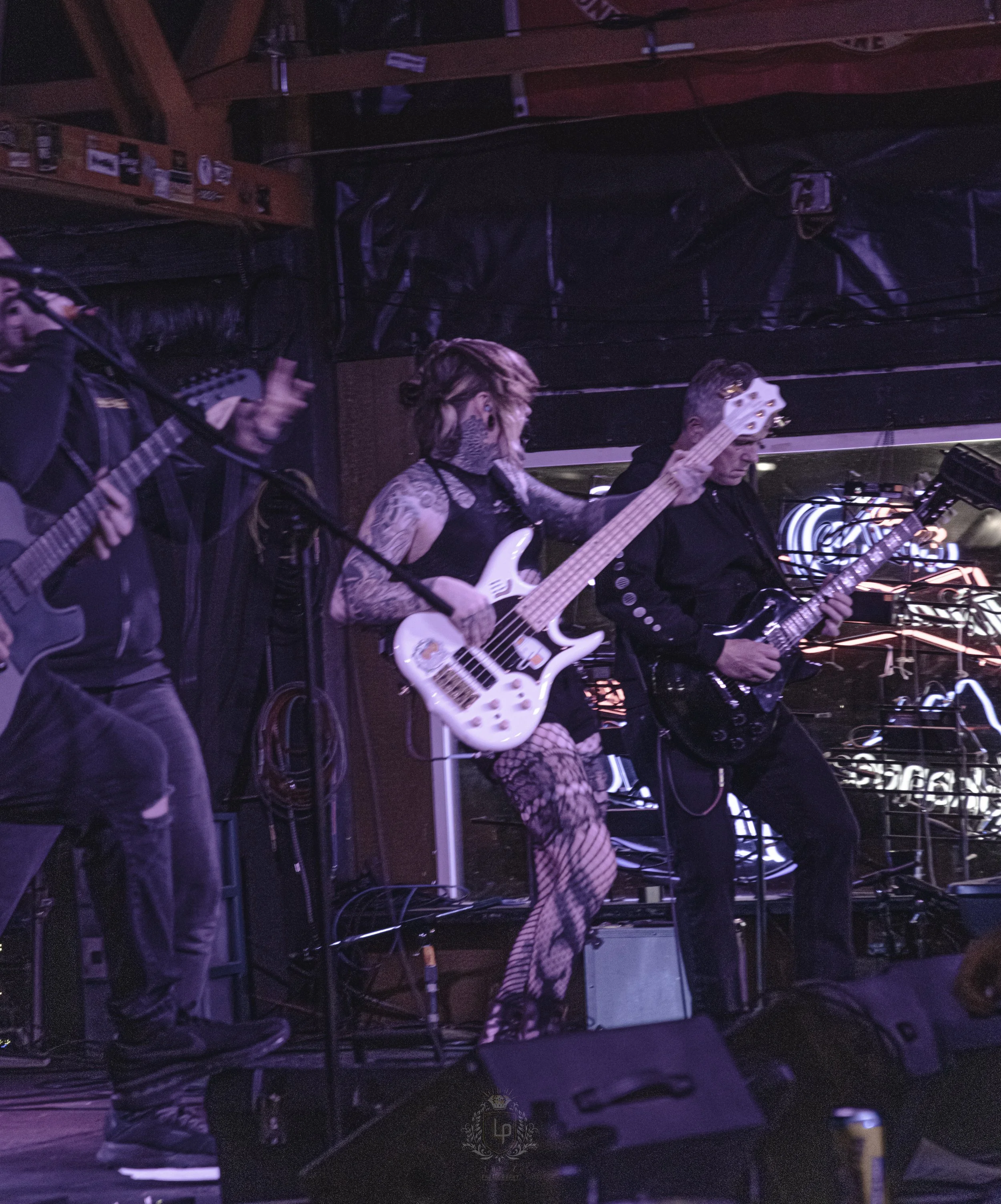 Musicians performing on stage with guitars, one woman with tattoos playing a bass guitar and wearing fishnet stockings.