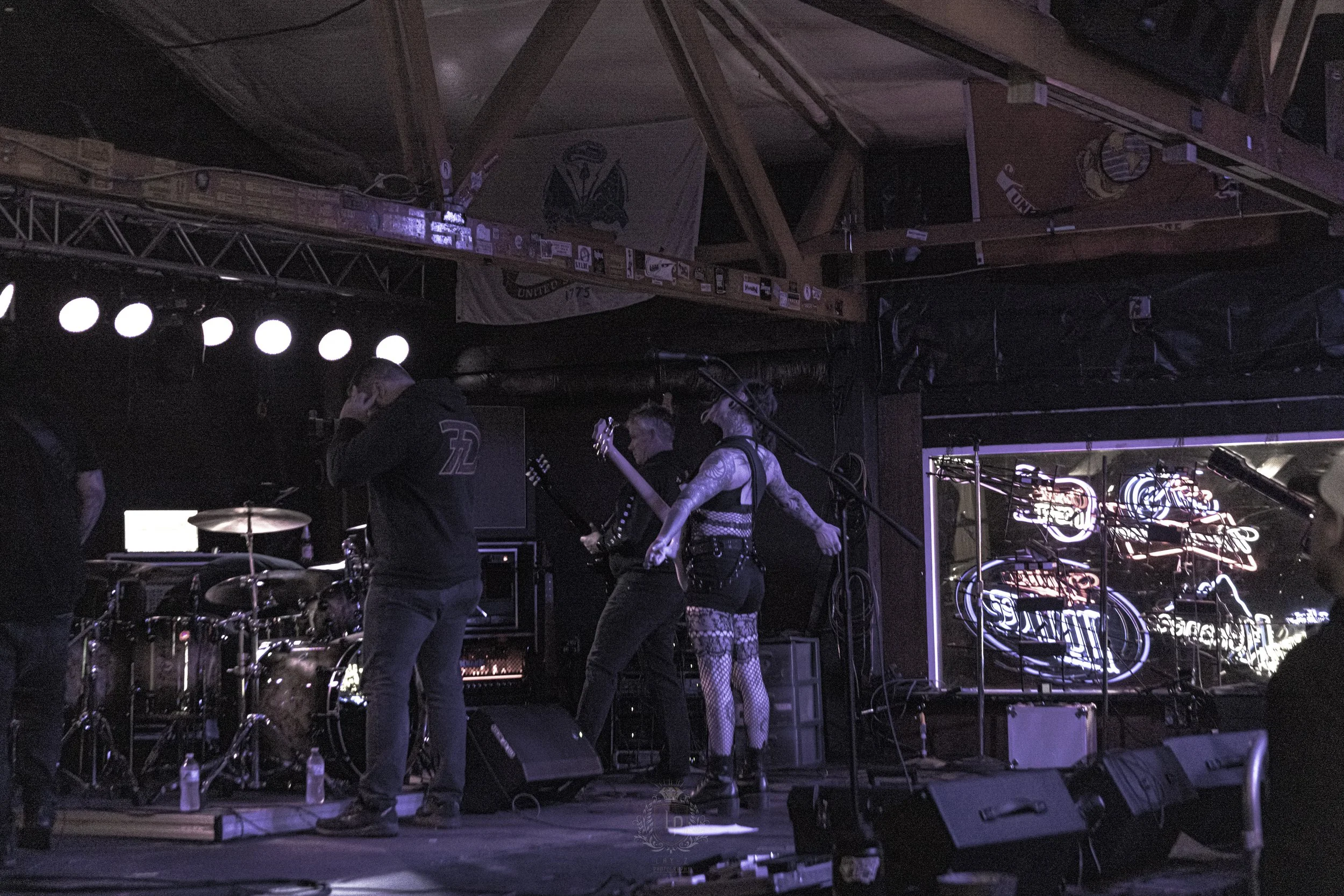 A band preparing to perform on stage in a dimly lit venue with neon signs and a neon sign in the background.