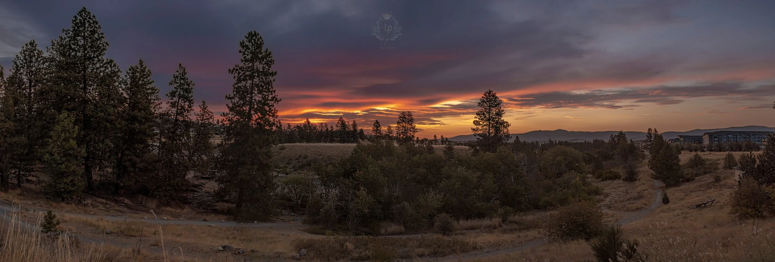 Sunset over a landscape with trees, rolling hills, and a cloudy sky.