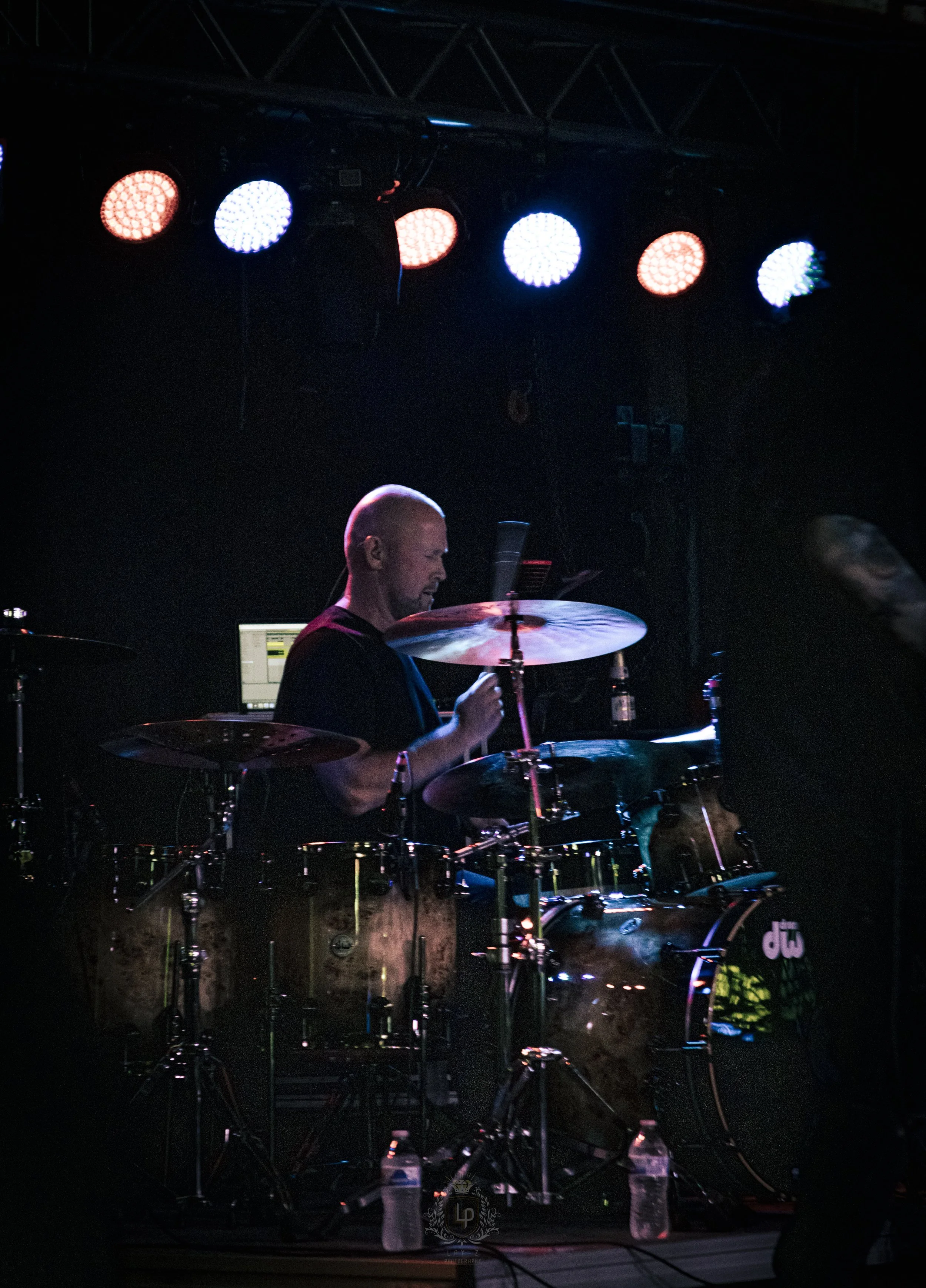 A drummer playing a drum set on stage under stage lights during a performance.