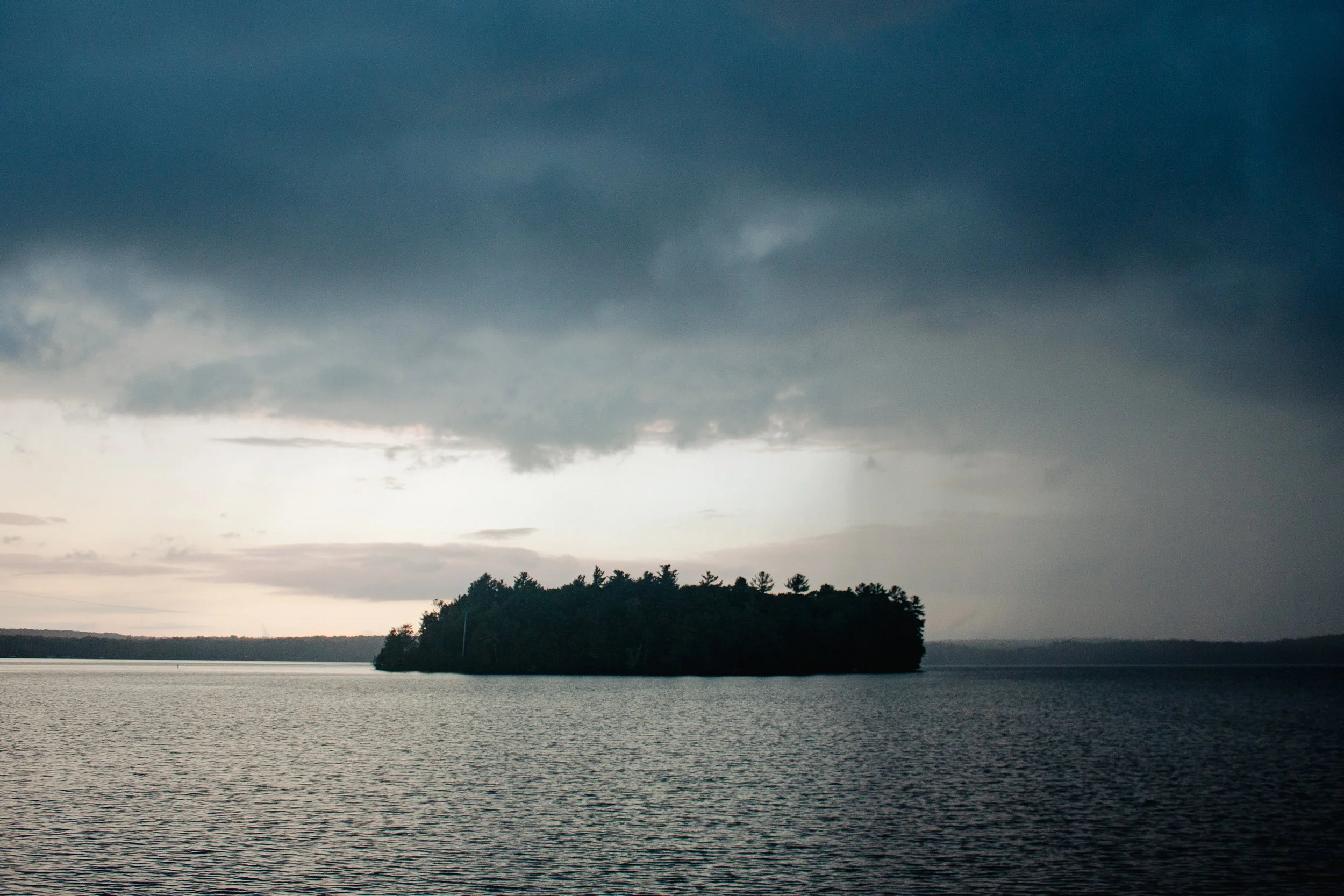 A large lake with an island covered in trees, under a dark cloudy sky.