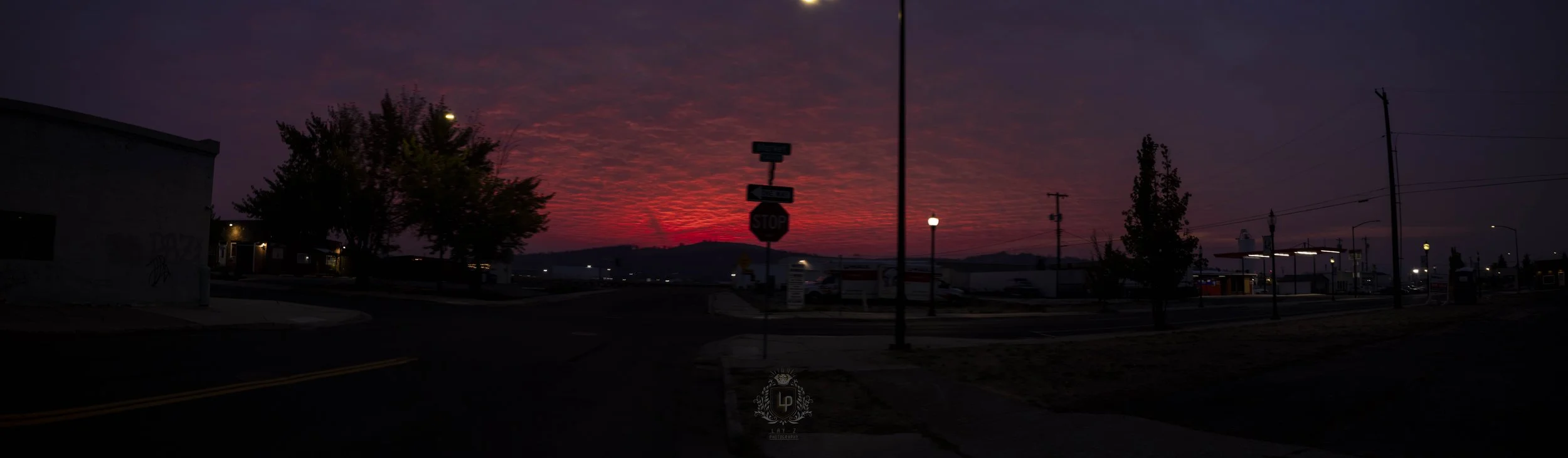 Colorful sunset sky over a suburban neighborhood with trees, streetlights, and power lines.