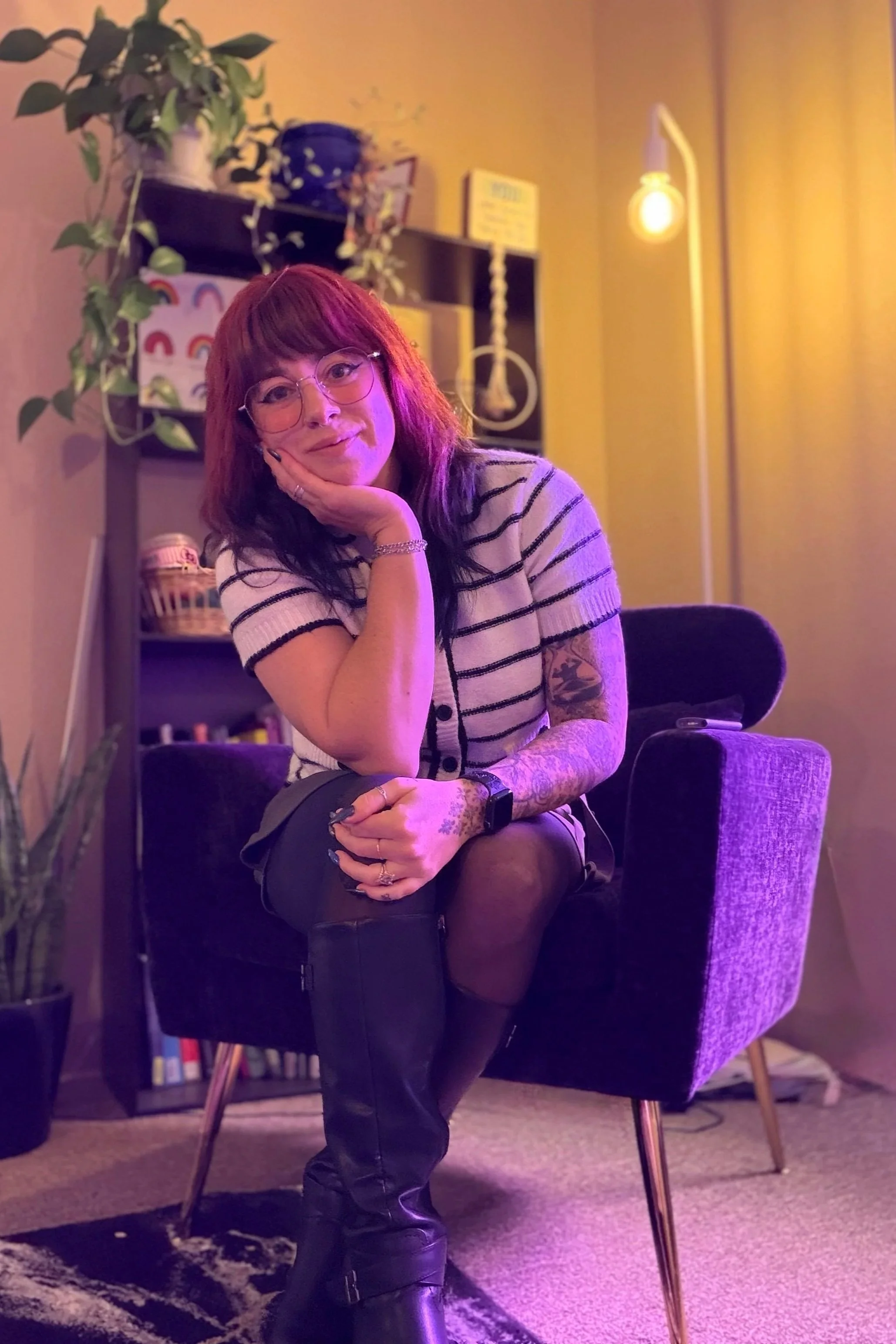 Dr. Adare Toral with red hair, glasses, and tattoos sitting on an armchair in a cozy, colorful room illuminated by a warm lamp.  AI therapy support, chatgpt, San Luis Obispo therapist. SLO therapy.  Downtown SLO mental health support.