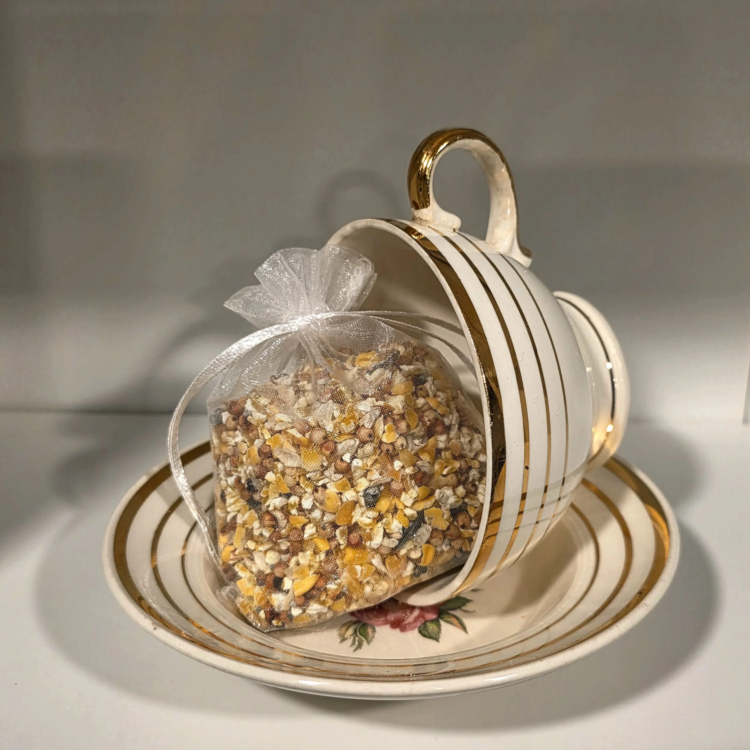 gold and cream tea cup with bird seed in white pouch