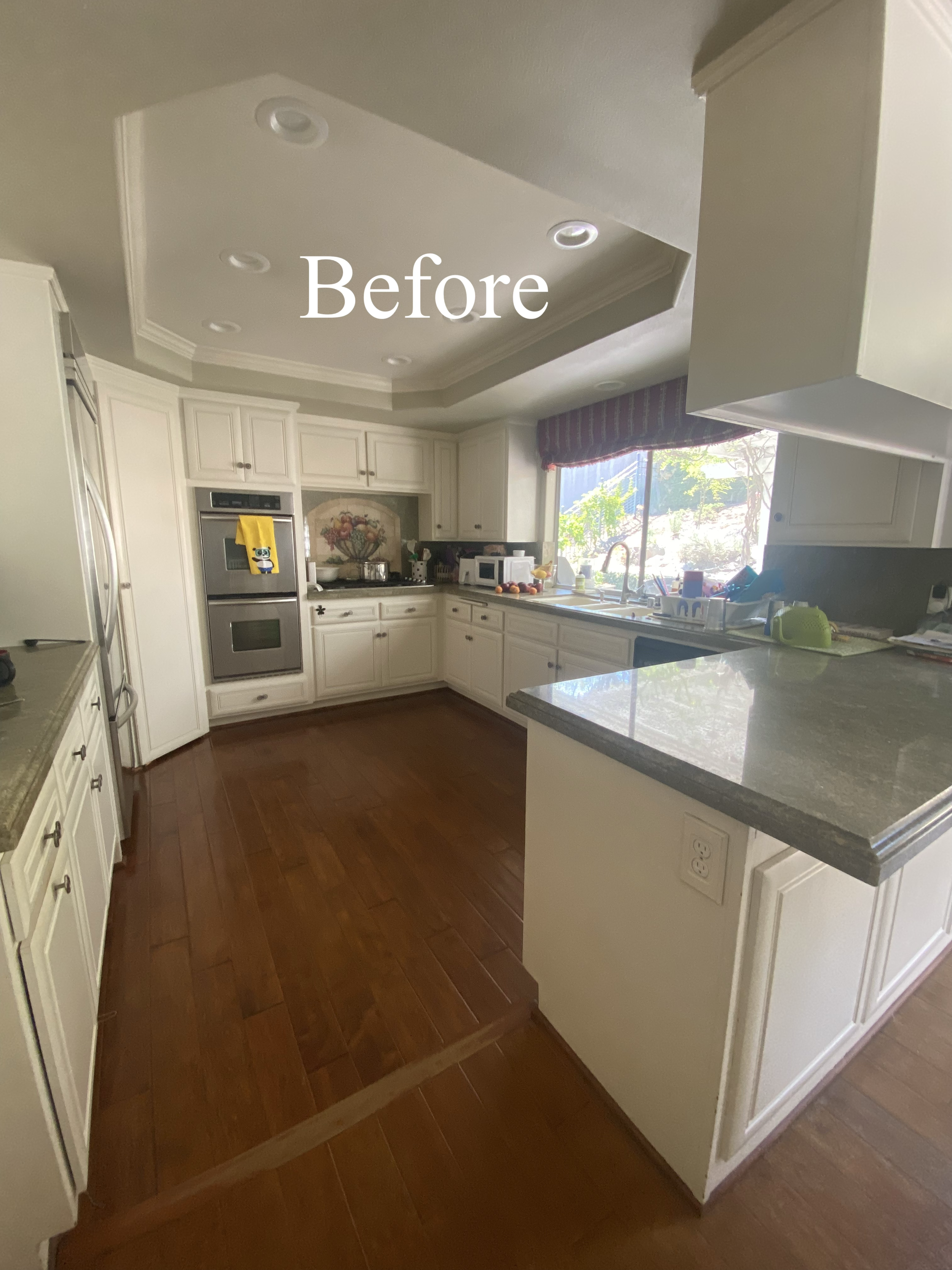 Kitchen with white cabinets, granite countertops, wooden floor, window with a view of trees, and the word 'Before' overlaid on the image.