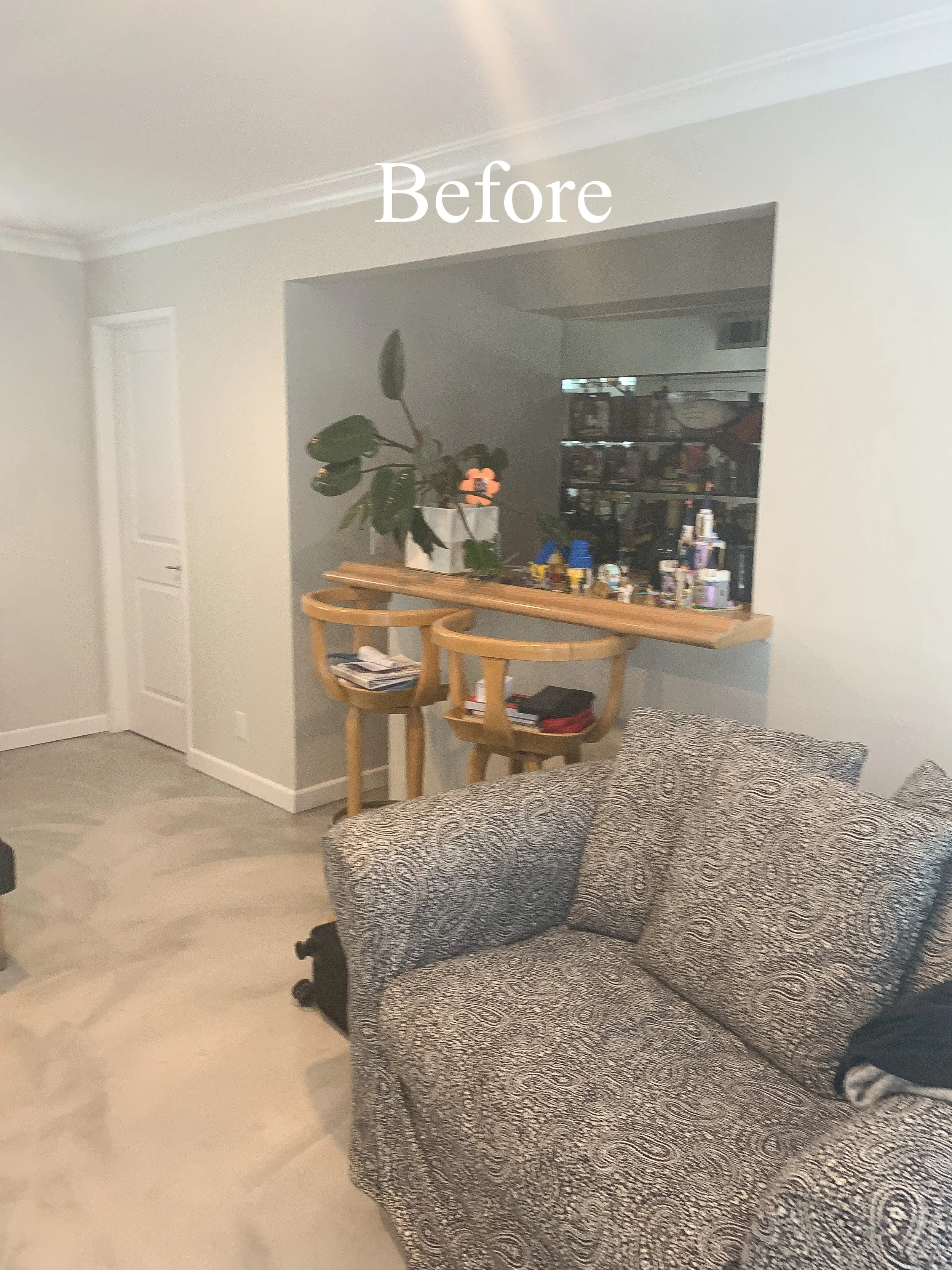 Living room with patterned sofa, in the background a countertop with a plant and various toys or objects, and two wooden bar stools.