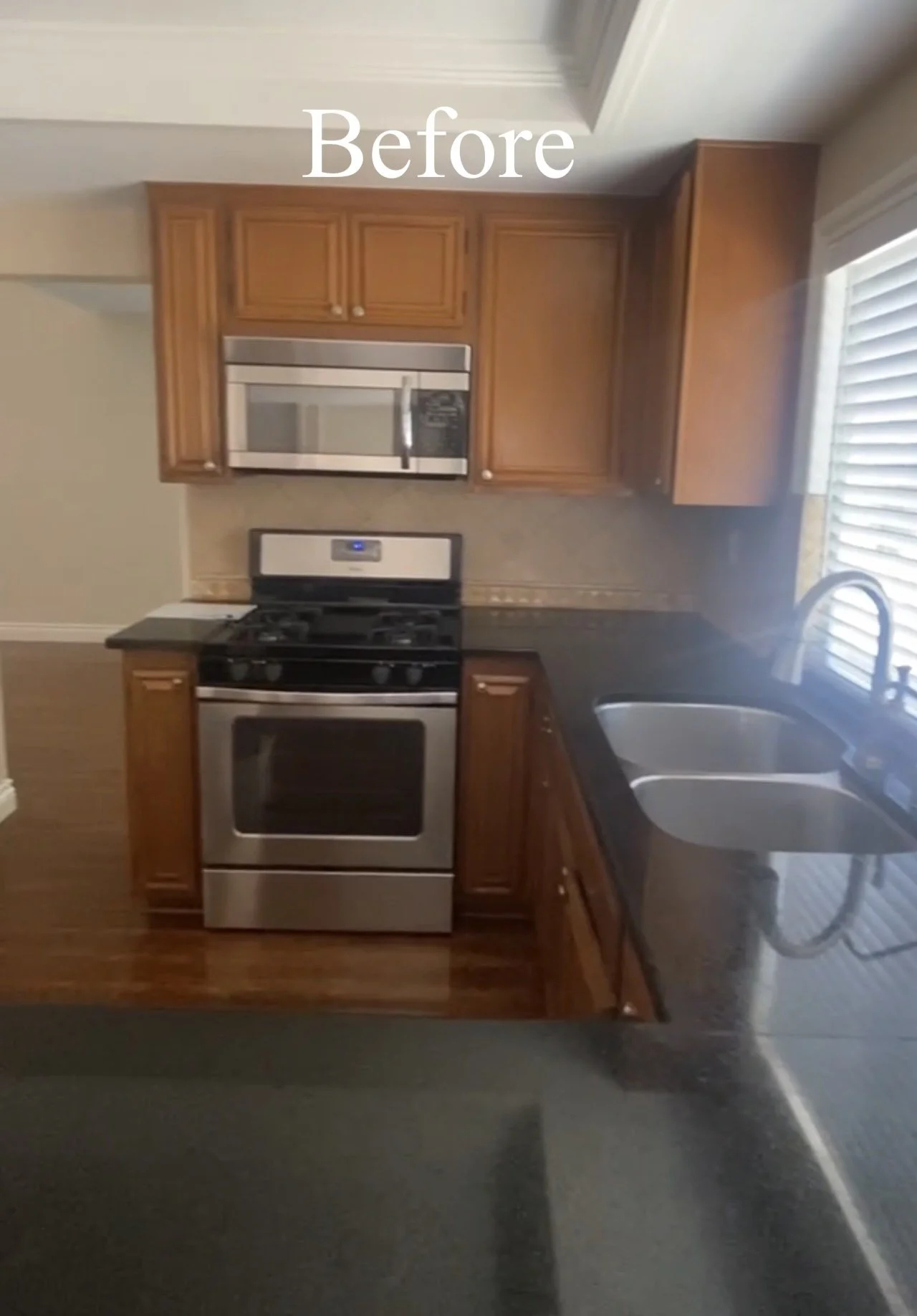 Kitchen with wooden cabinets, microwave above stove, stainless steel oven, black countertop, and double sink near window. Text 'Before' at the top.