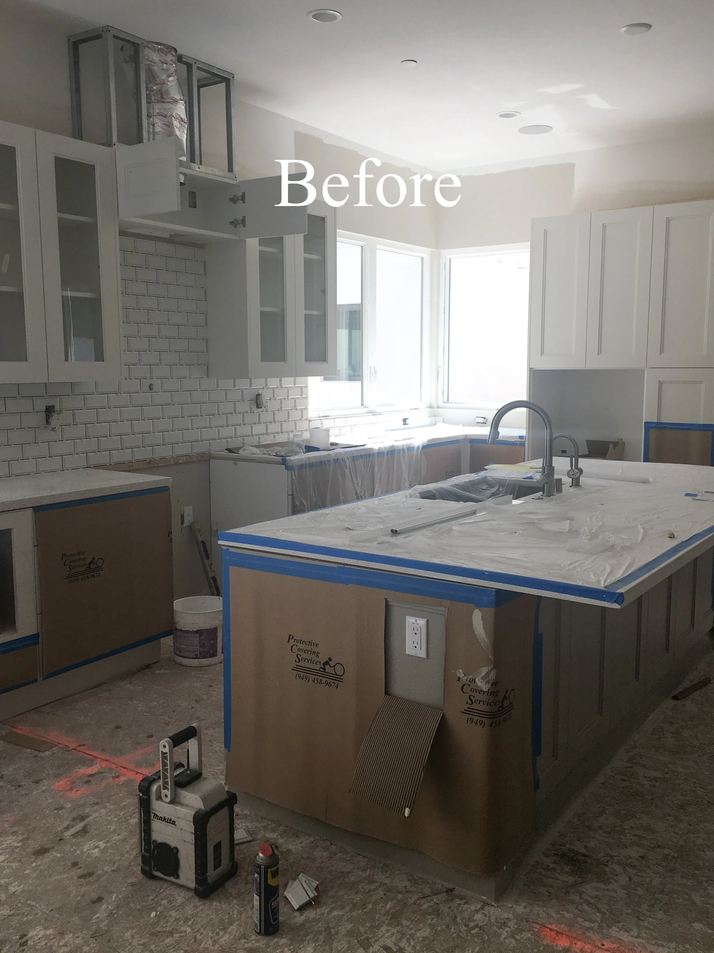 Kitchen under renovation with white cabinets, a white subway tile backsplash, an island covered in protective wrapping, and construction tools on the floor. The word 'Before' is overlaid on the image.