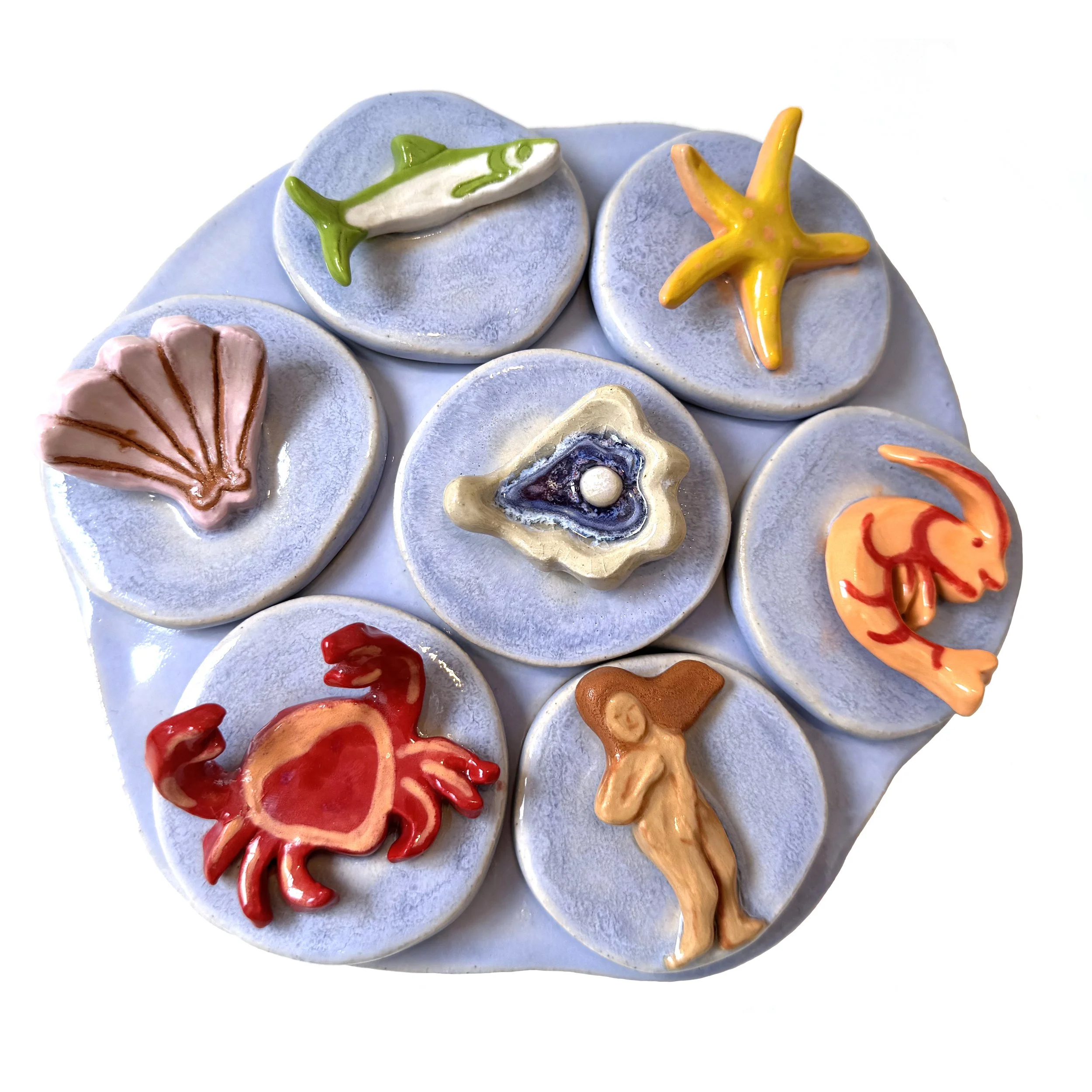 Collection of seven ceramic tiles with sea-themed and human figures, each on round blue-gray backgrounds. 
