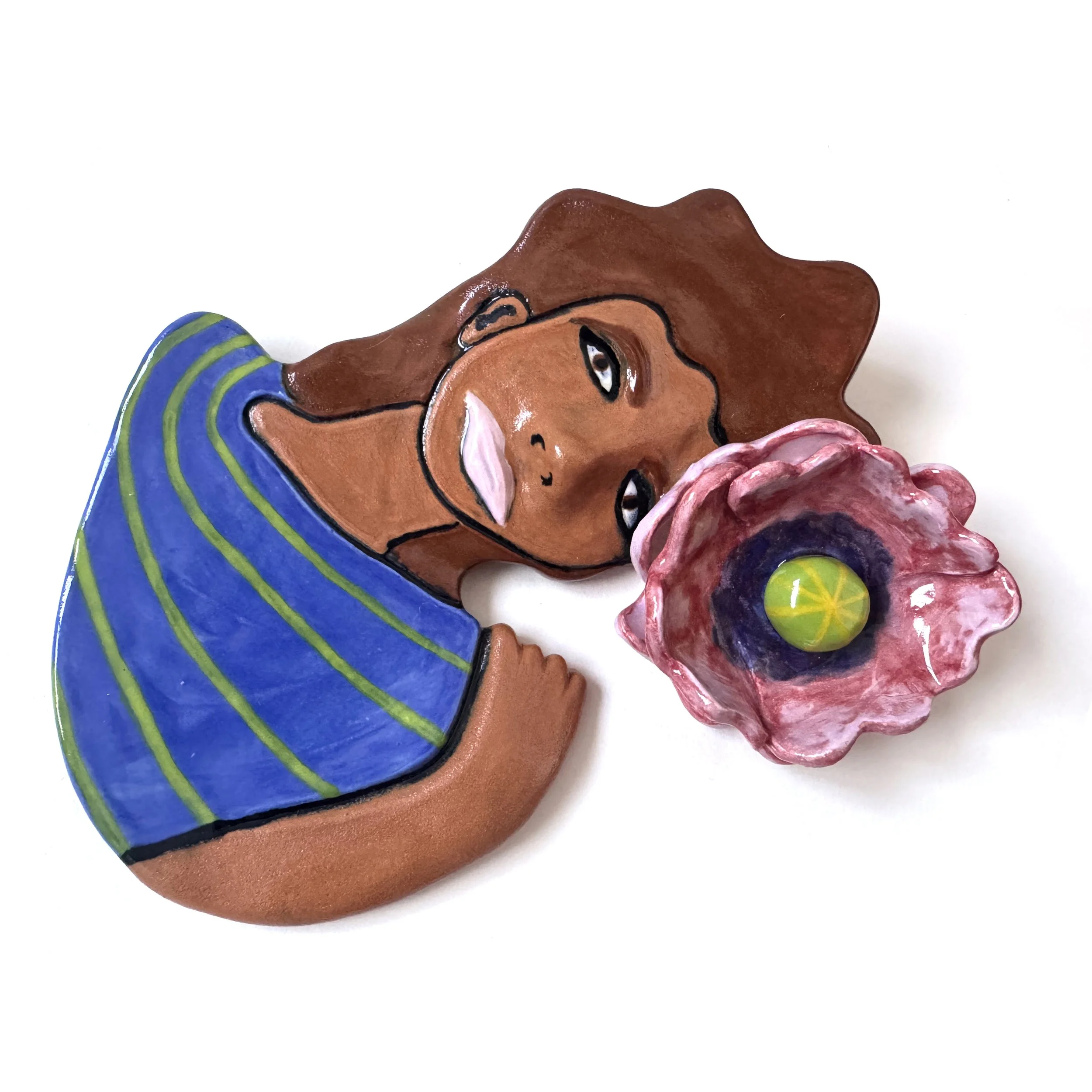 Decorative art piece of a woman with brown hair wearing a striped blue and green shirt, lying next to a pink and purple flower with a yellow center.